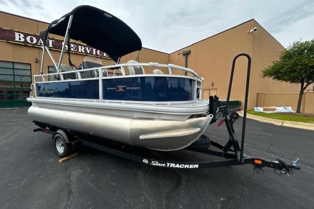 2026 Sun Tracker Bass Buggy 18 DLX pontoon boat on trailer outside service center.