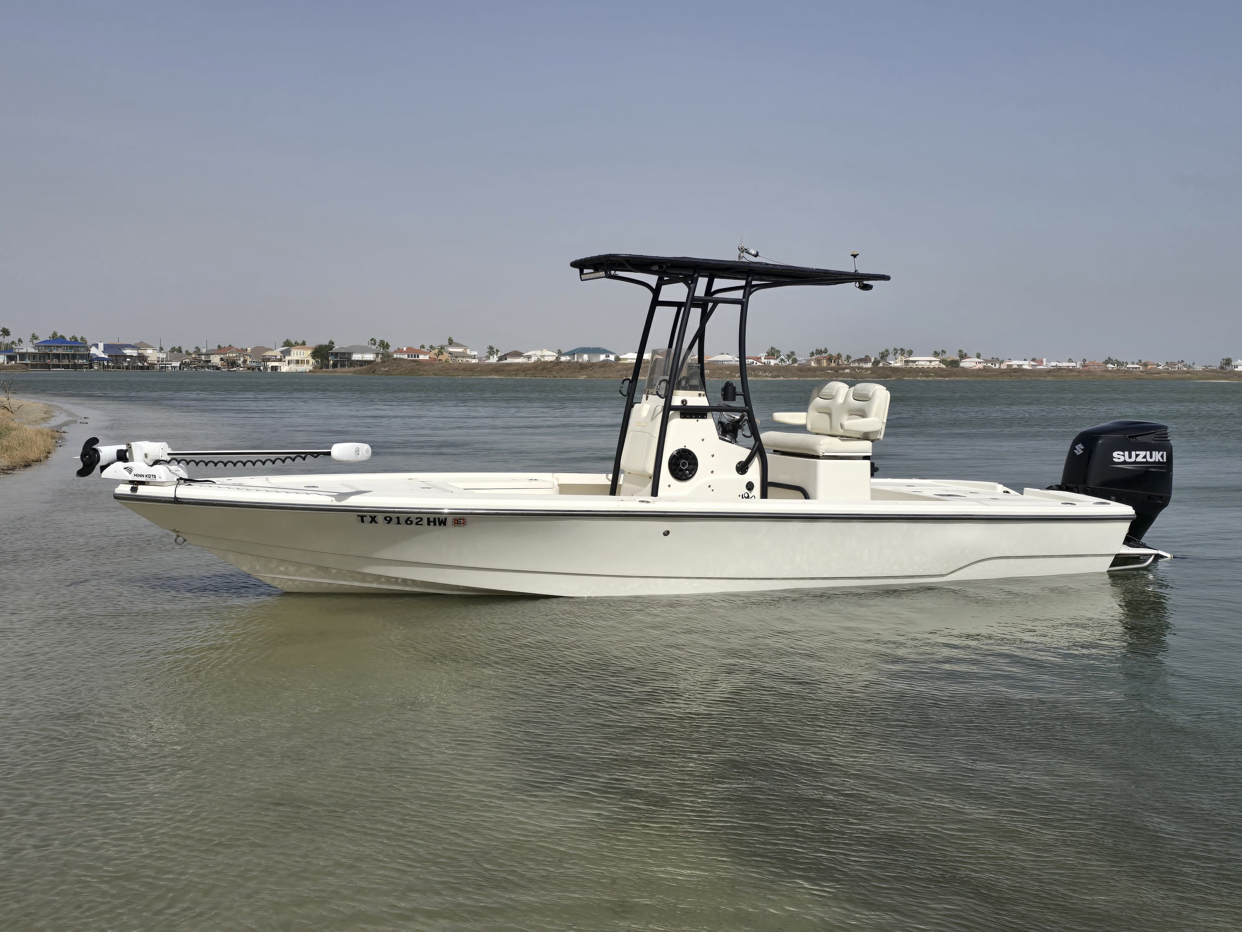 A white boat with a black canopy on calm water, houses in the background.