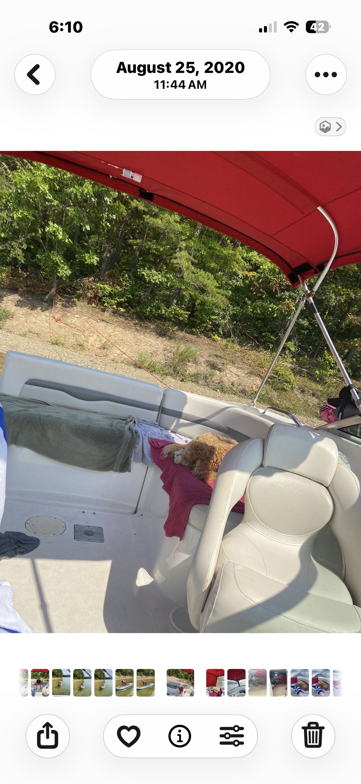 A boat with a red sunshade and white seats. A dog is lying on a seat.
