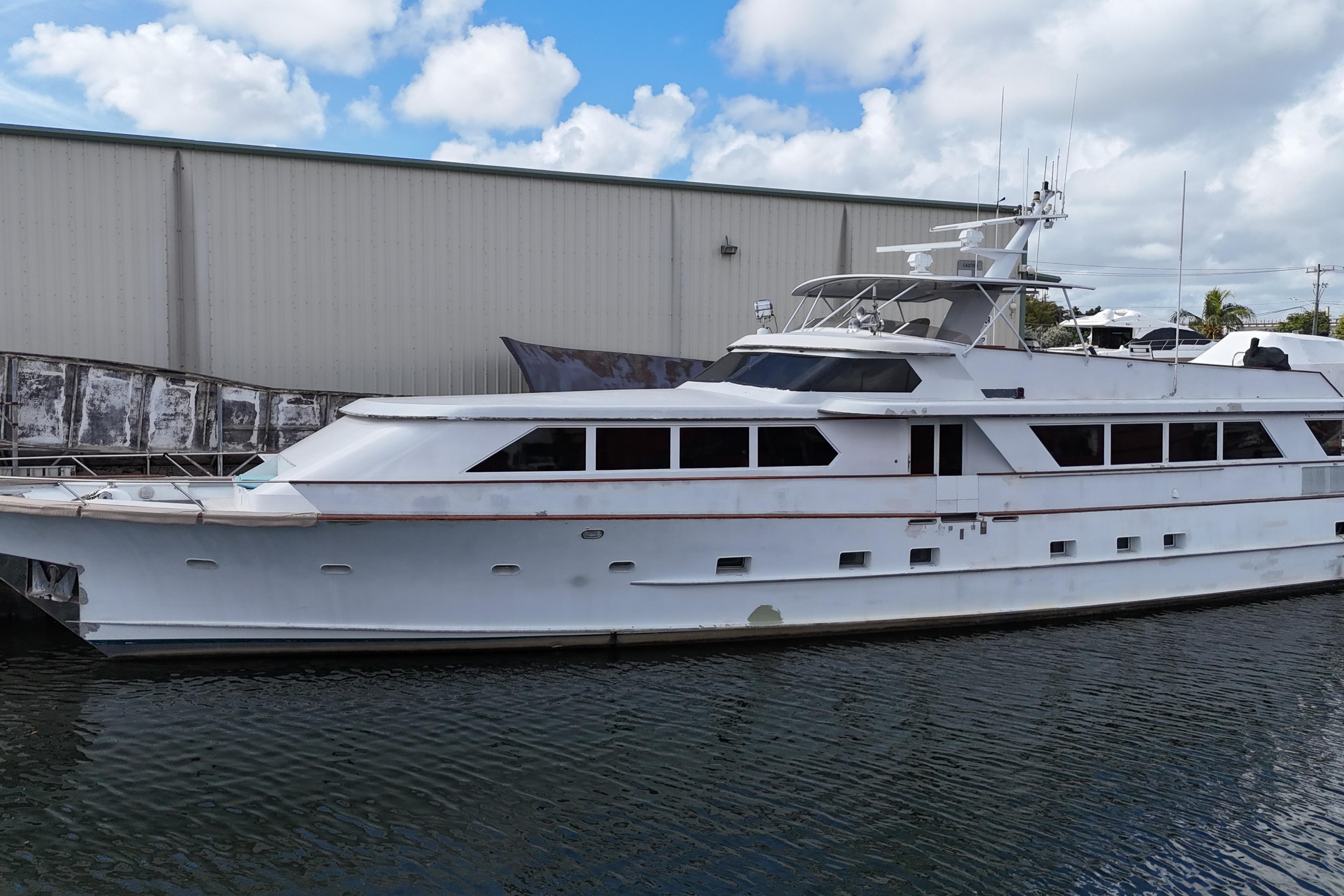 Luxury 1990 Denison 109 yacht docked by a warehouse under a partly cloudy sky.