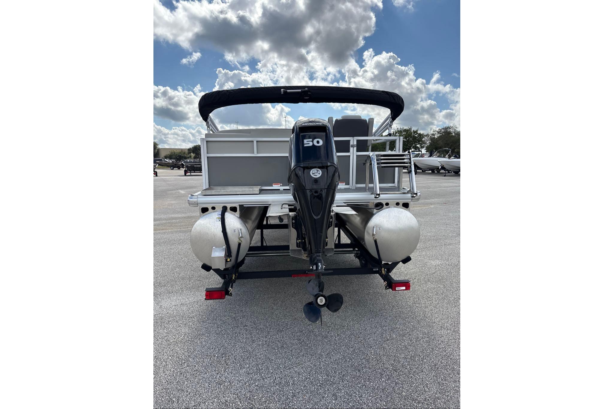 2026 Sun Tracker Bass Buggy 16 XL Select pontoon boat, rear view with motor, under cloudy sky.