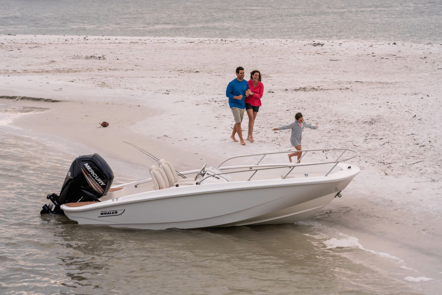 A family walks on the beach beside a Boston Whaler 160 Super Sport boat.