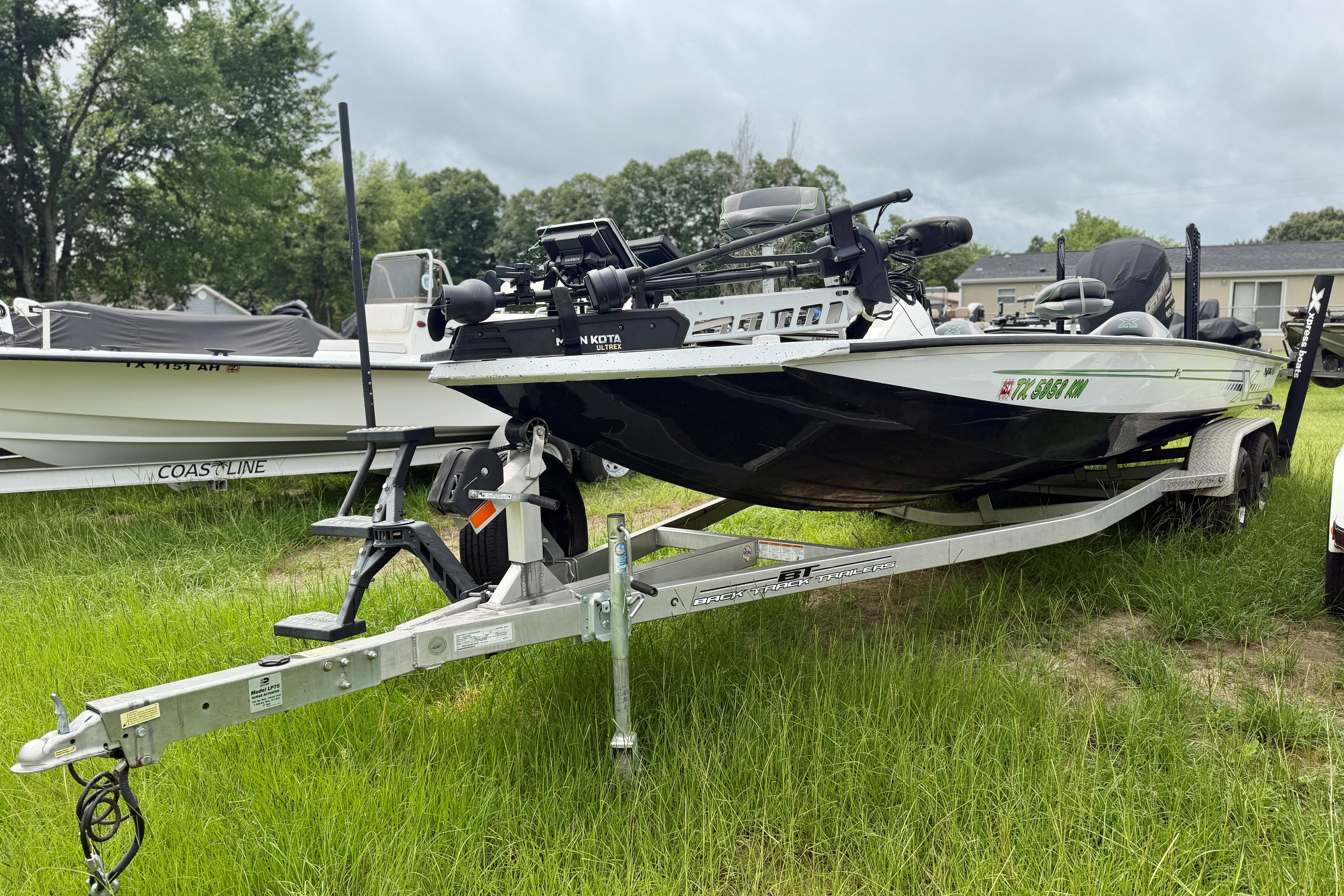 2022 Xpress X21 Pro boat on trailer, parked on grass, with trees in the background.