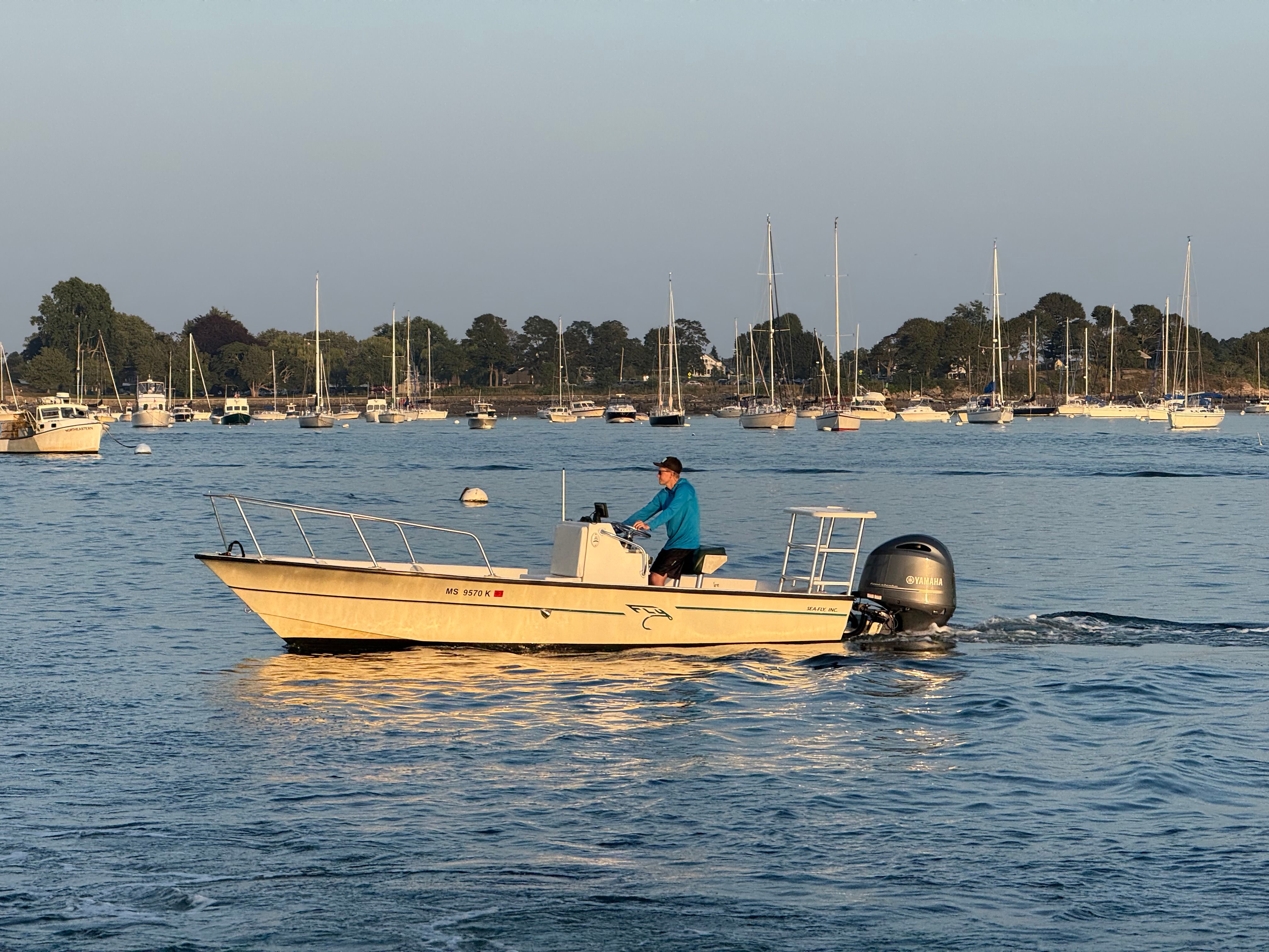A 2004 Custom Sea Fly boat cruising on a calm lake with numerous sailboats.