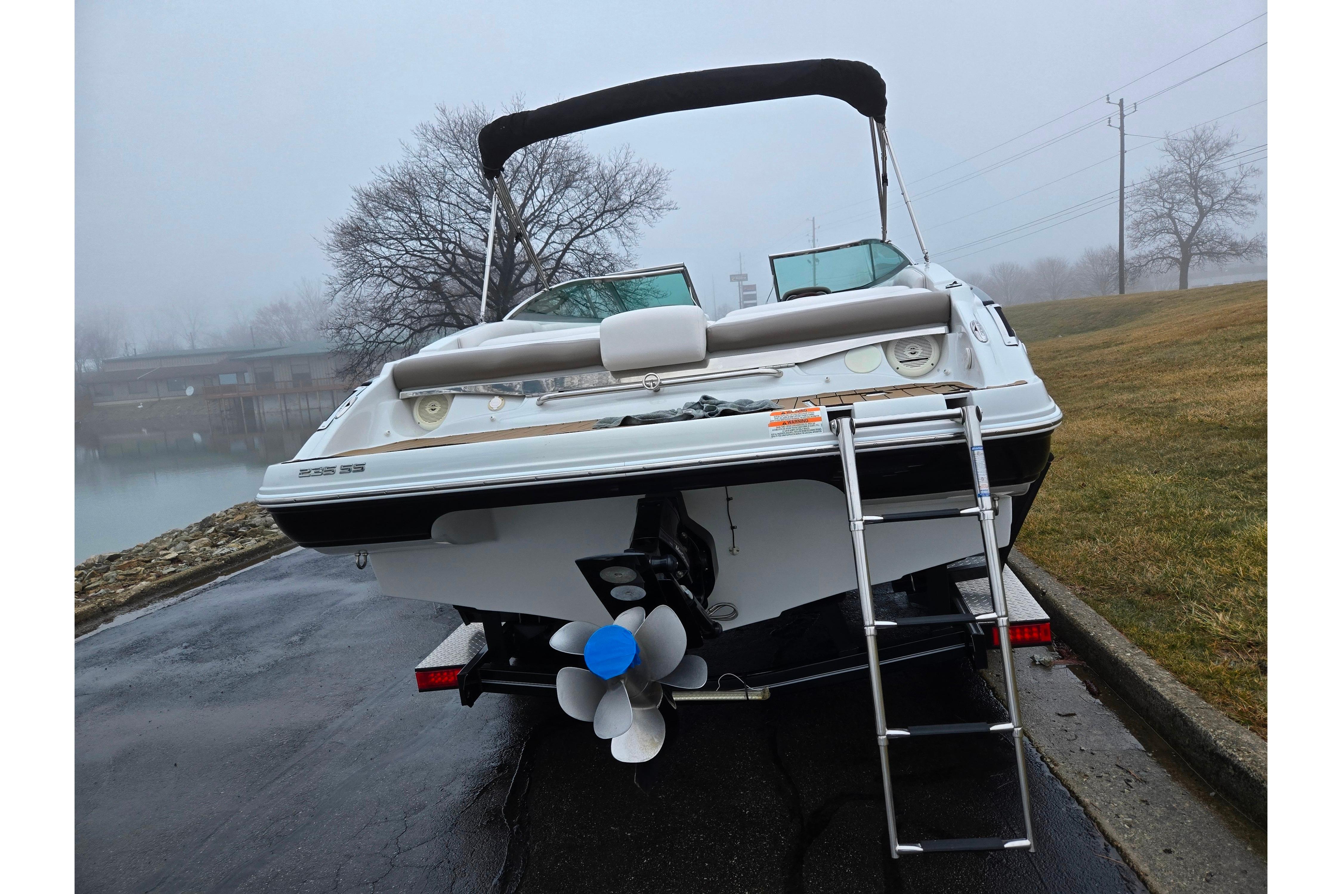 2012 Crownline 235 SS boat with ladder, parked on a wet road near a foggy lake.