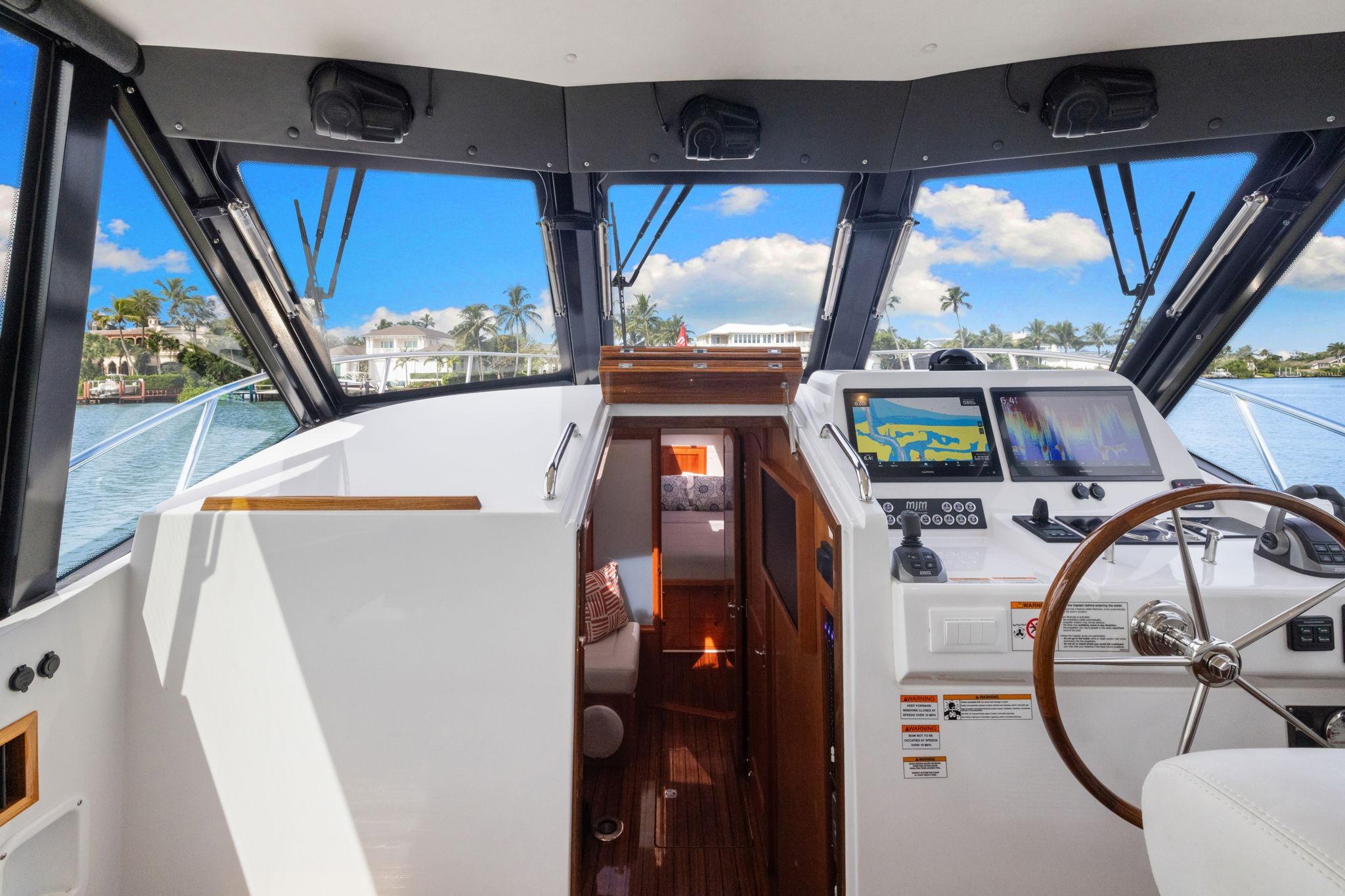 2024 MJM 42 yacht cockpit with navigation screens, steering wheel, and scenic water view.