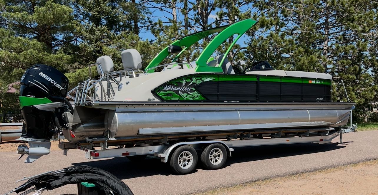 A 2020 Manitou 27 X-Plode SHP pontoon boat on a trailer, surrounded by trees.