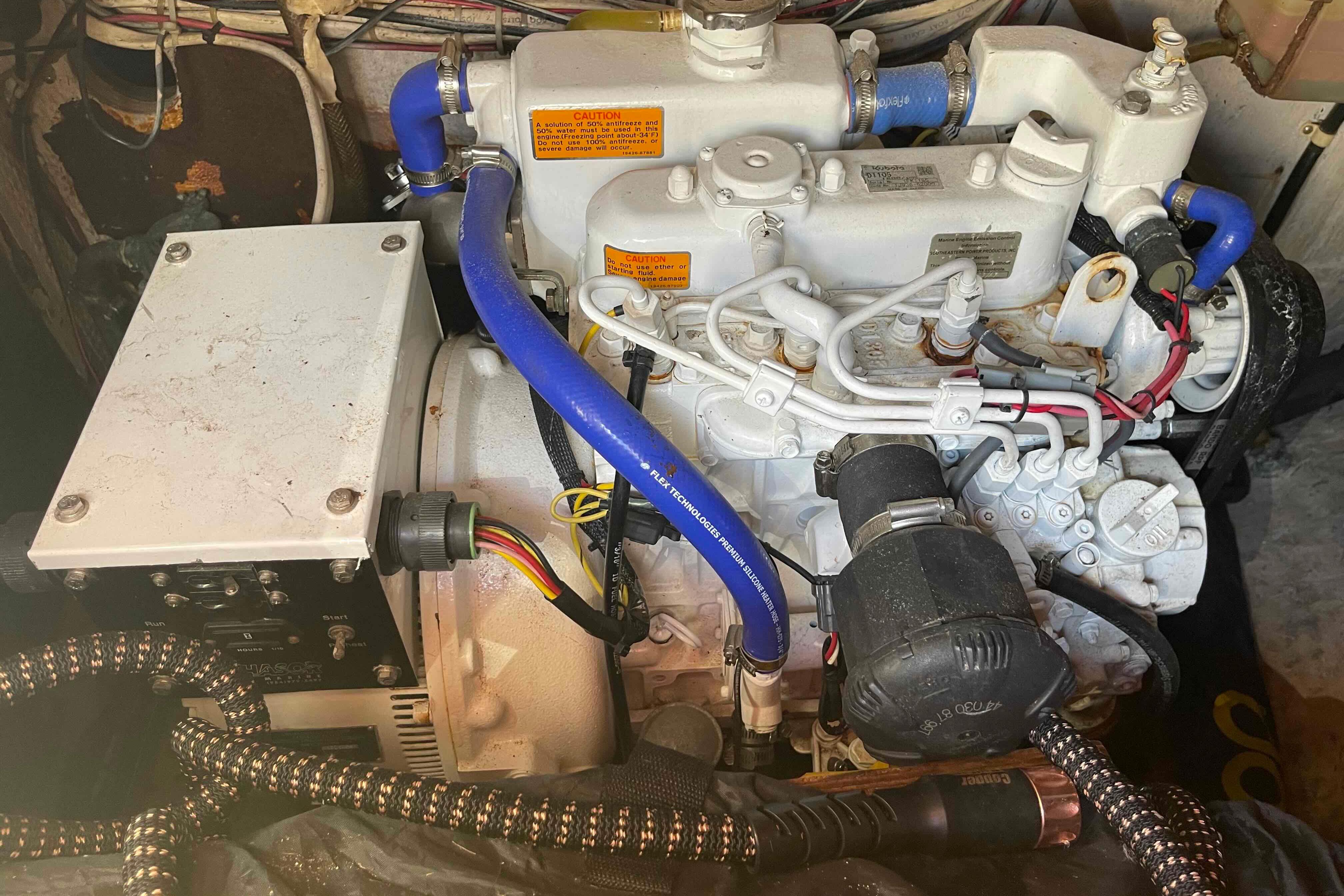 Engine compartment of a 1989 Island Packet 35 sailboat, featuring blue hoses and wiring.