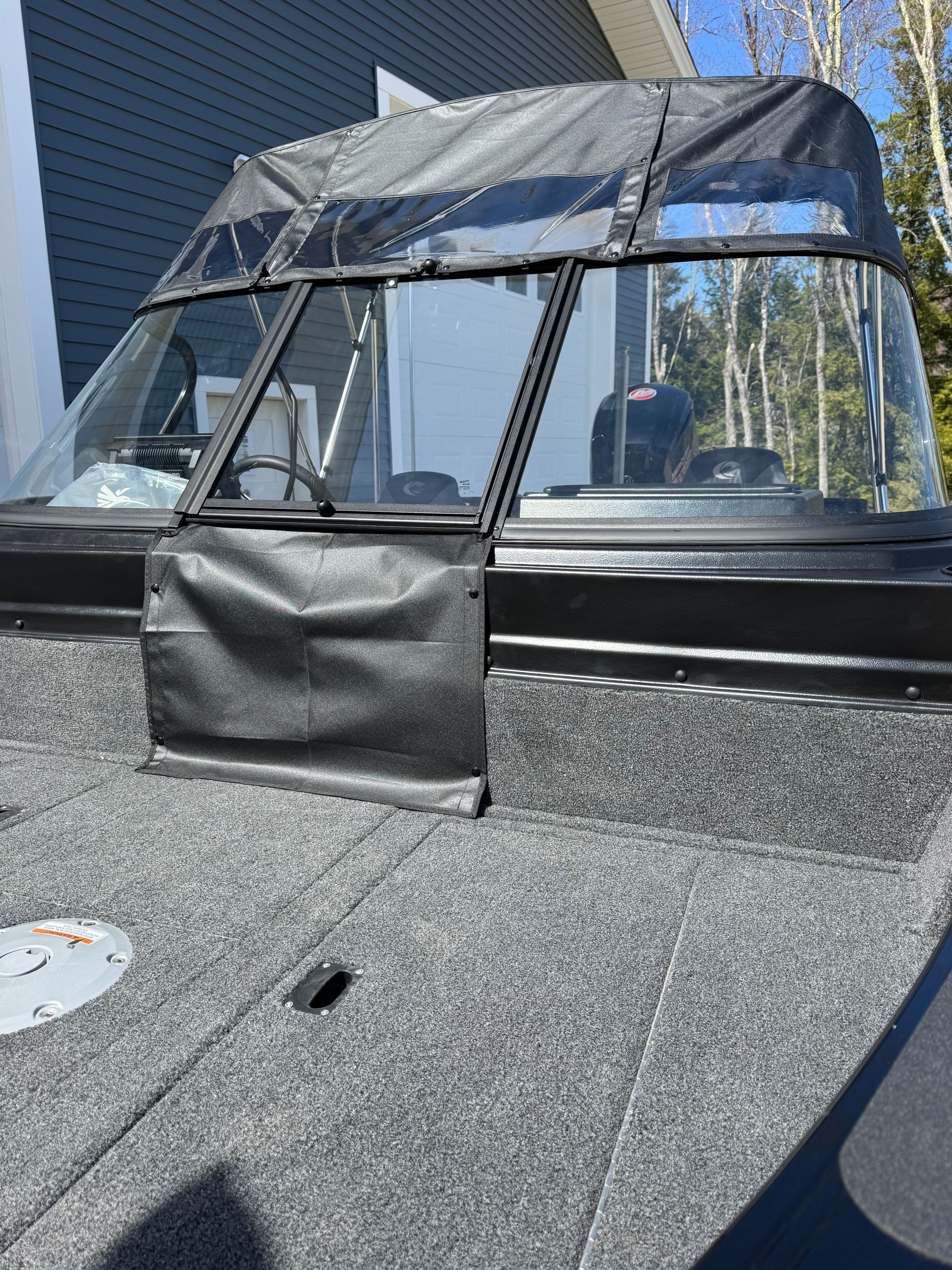 A modern fishing boat with gray carpeting and black canopy, parked in front of a building.
