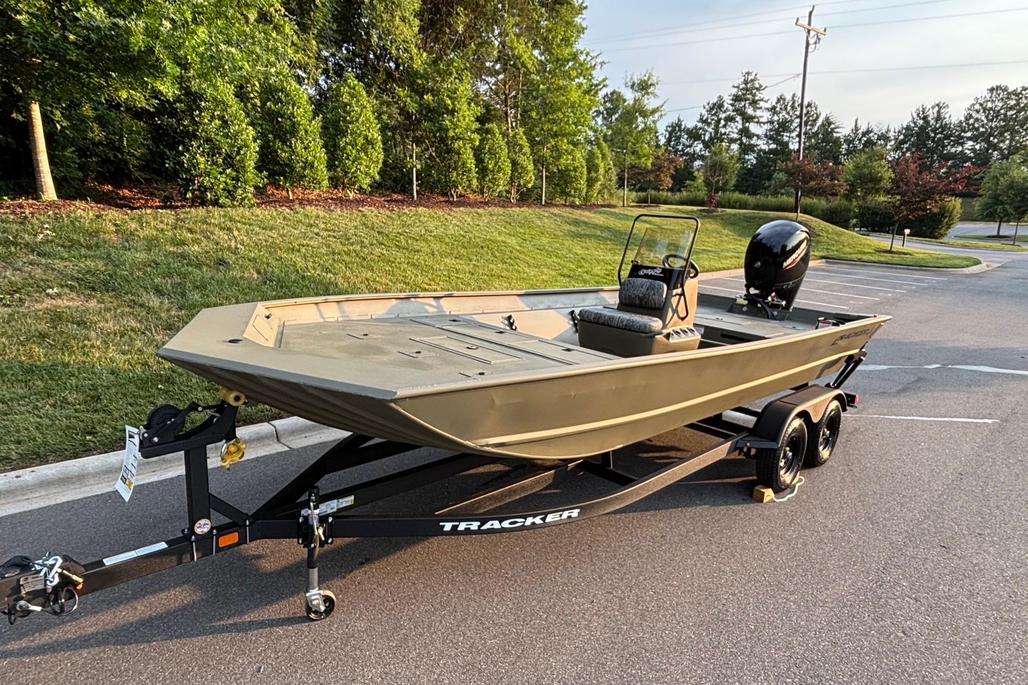 2026 Tracker Grizzly 2072 CC boat on trailer, parked outdoors, surrounded by greenery.