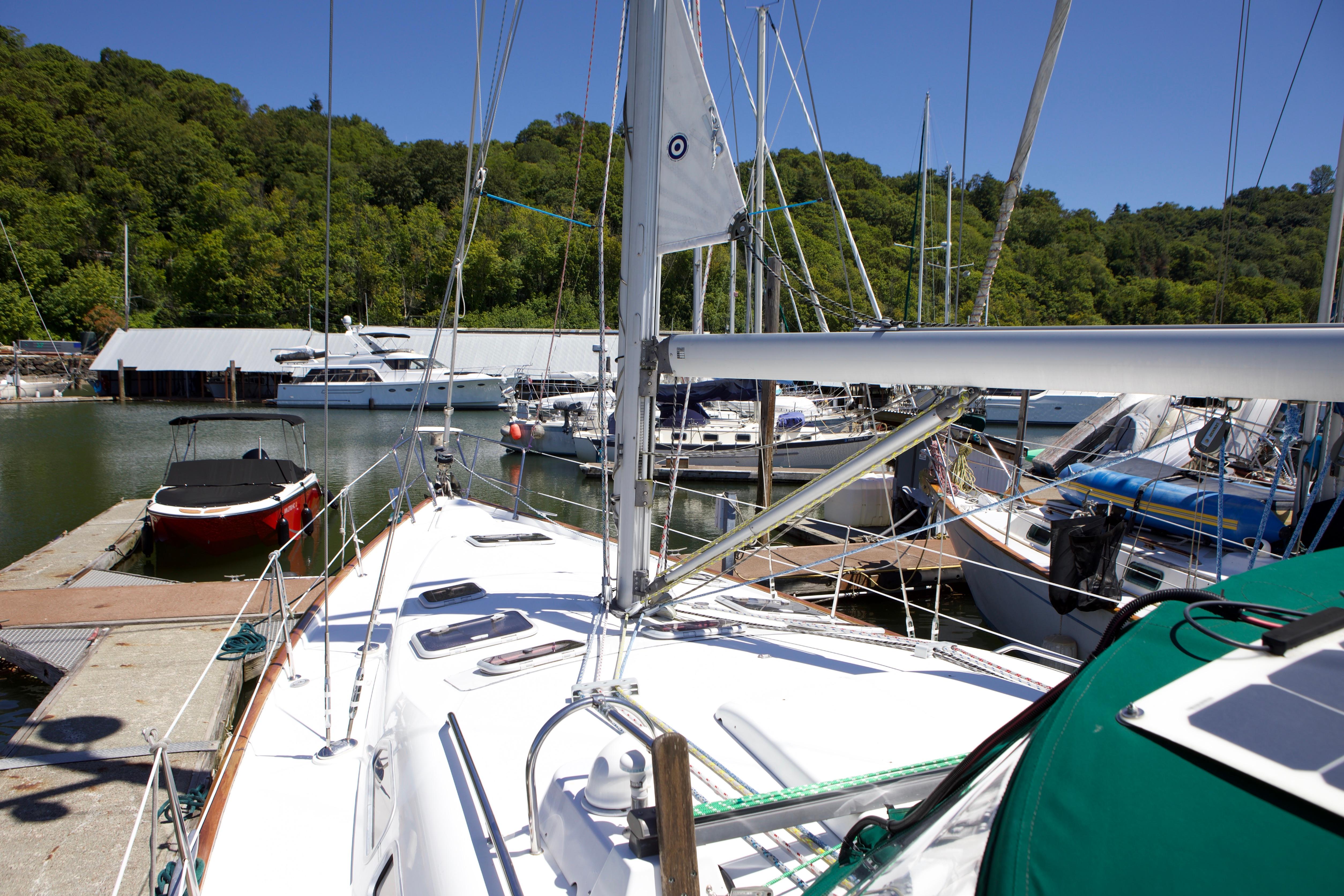 Sailboat Beneteau 423 (2005) docked at marina with lush green backdrop.