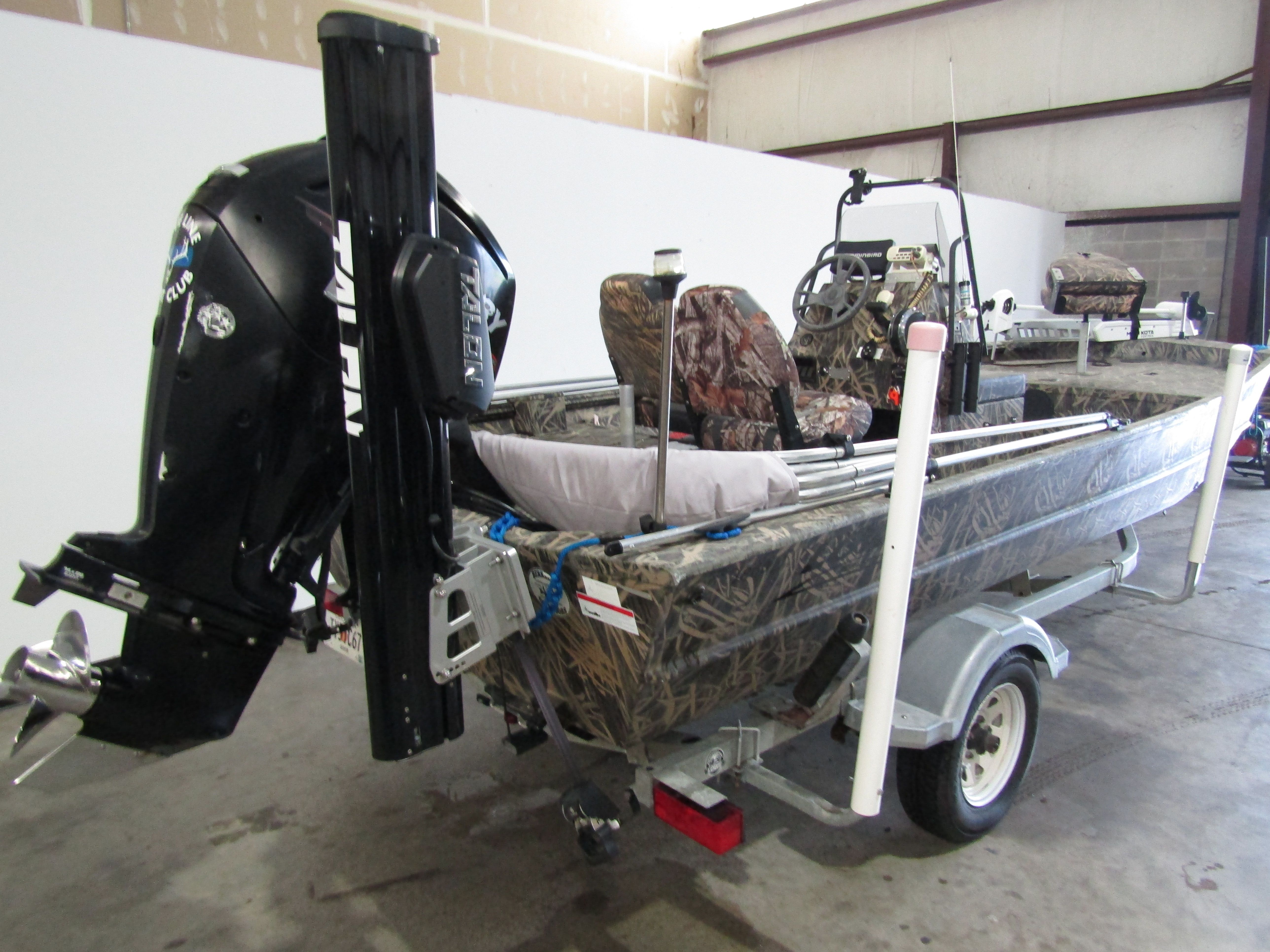 A 2016 Lowe 186 boat in a warehouse. It features an outboard motor and camouflage seats.