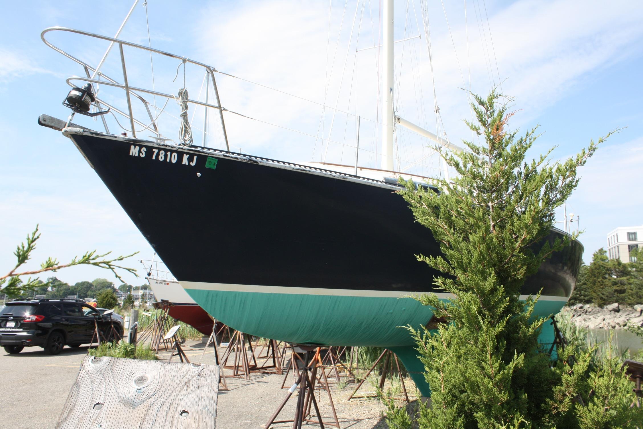 1981 S2 9.2A sailboat on stands, partially obscured by greenery, in a boatyard setting.