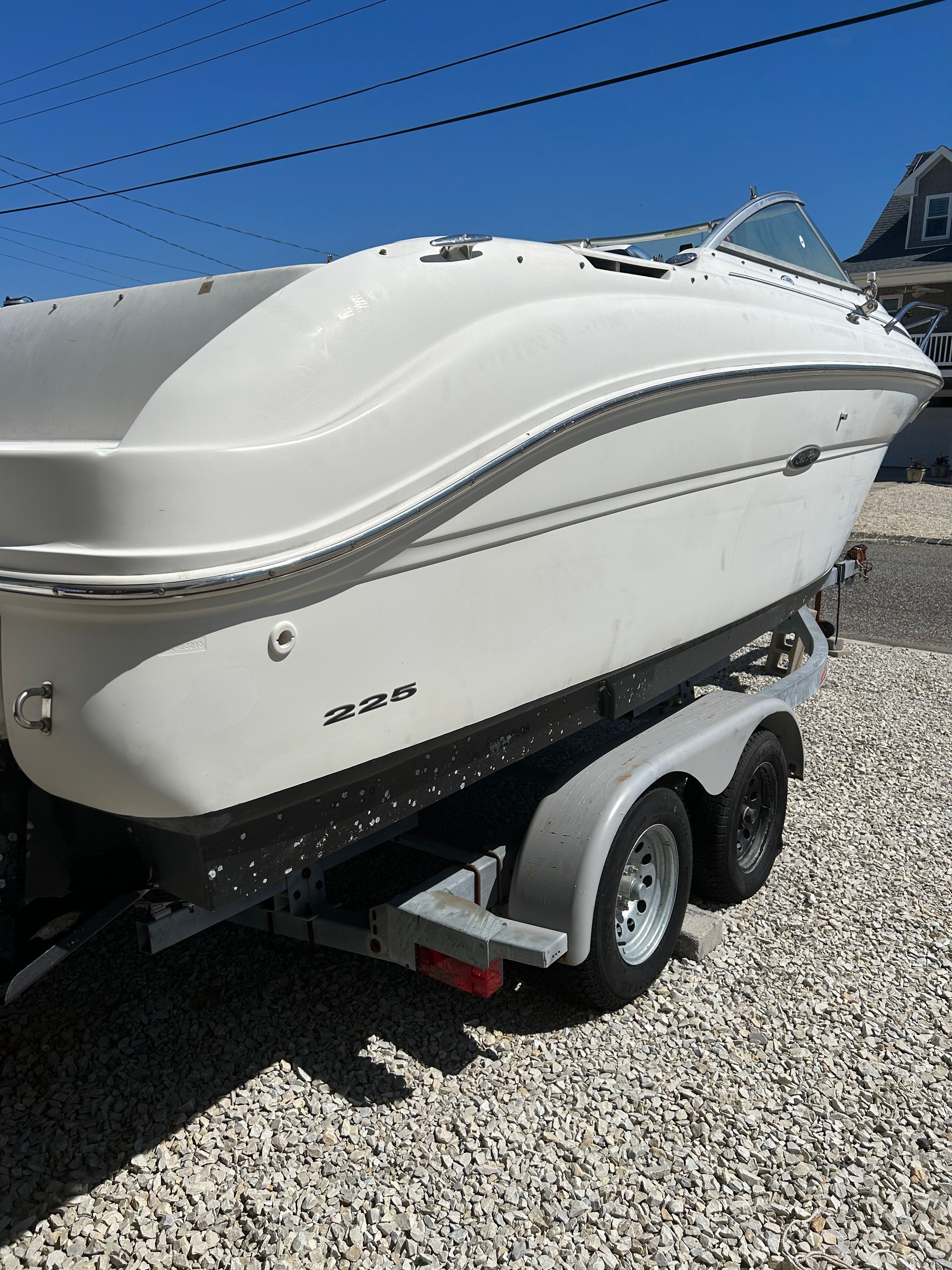 A white 2002 Sea Ray 225 Weekender boat on a trailer in a gravel lot.
