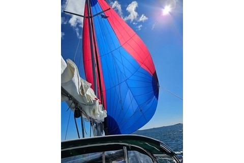 Beneteau Oceanis 321 sailboat with vibrant red and blue spinnaker under sunny skies.