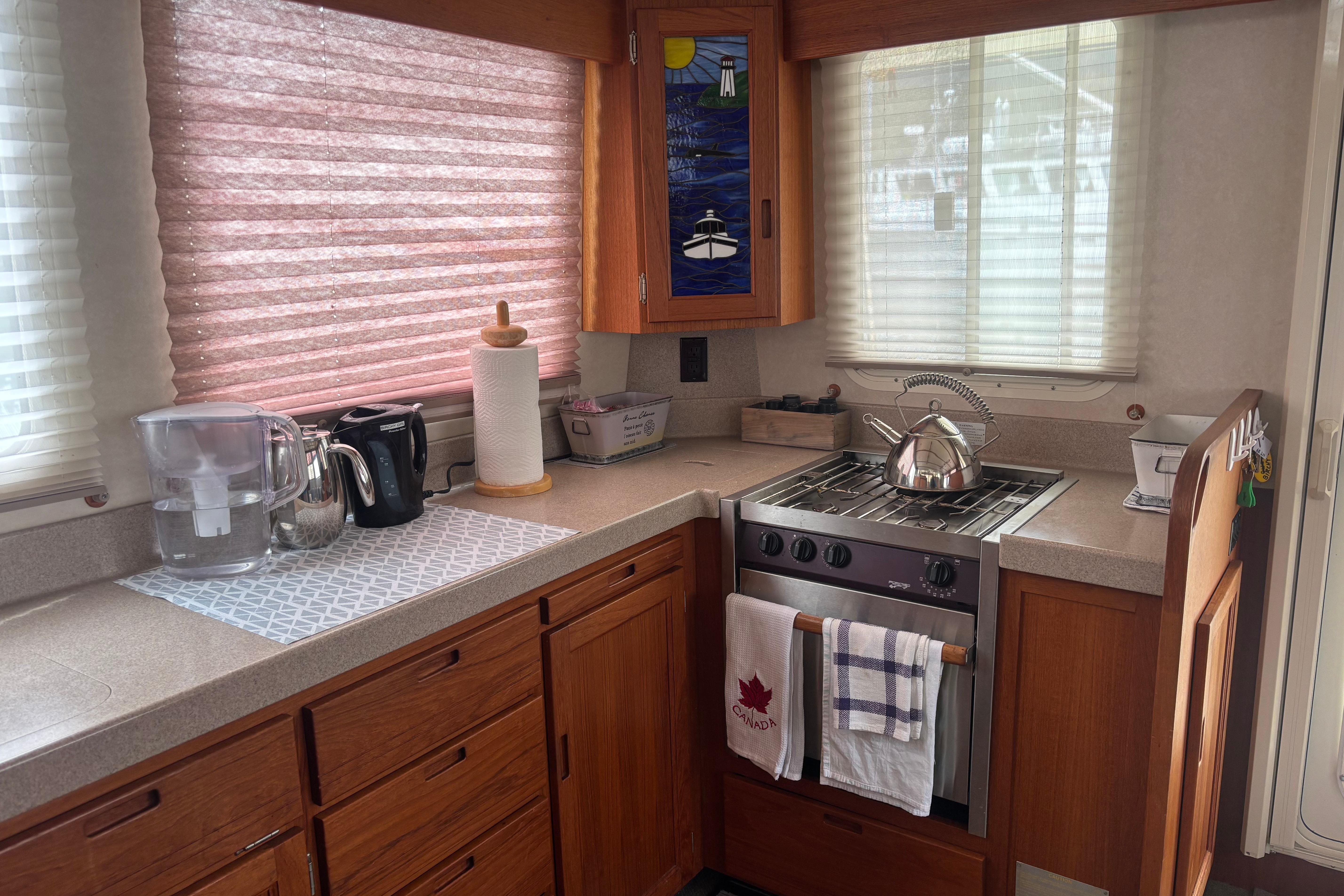 Cozy kitchen in a 2004 Nordic Tug 37 boat with stove, kettle, and wooden cabinetry.