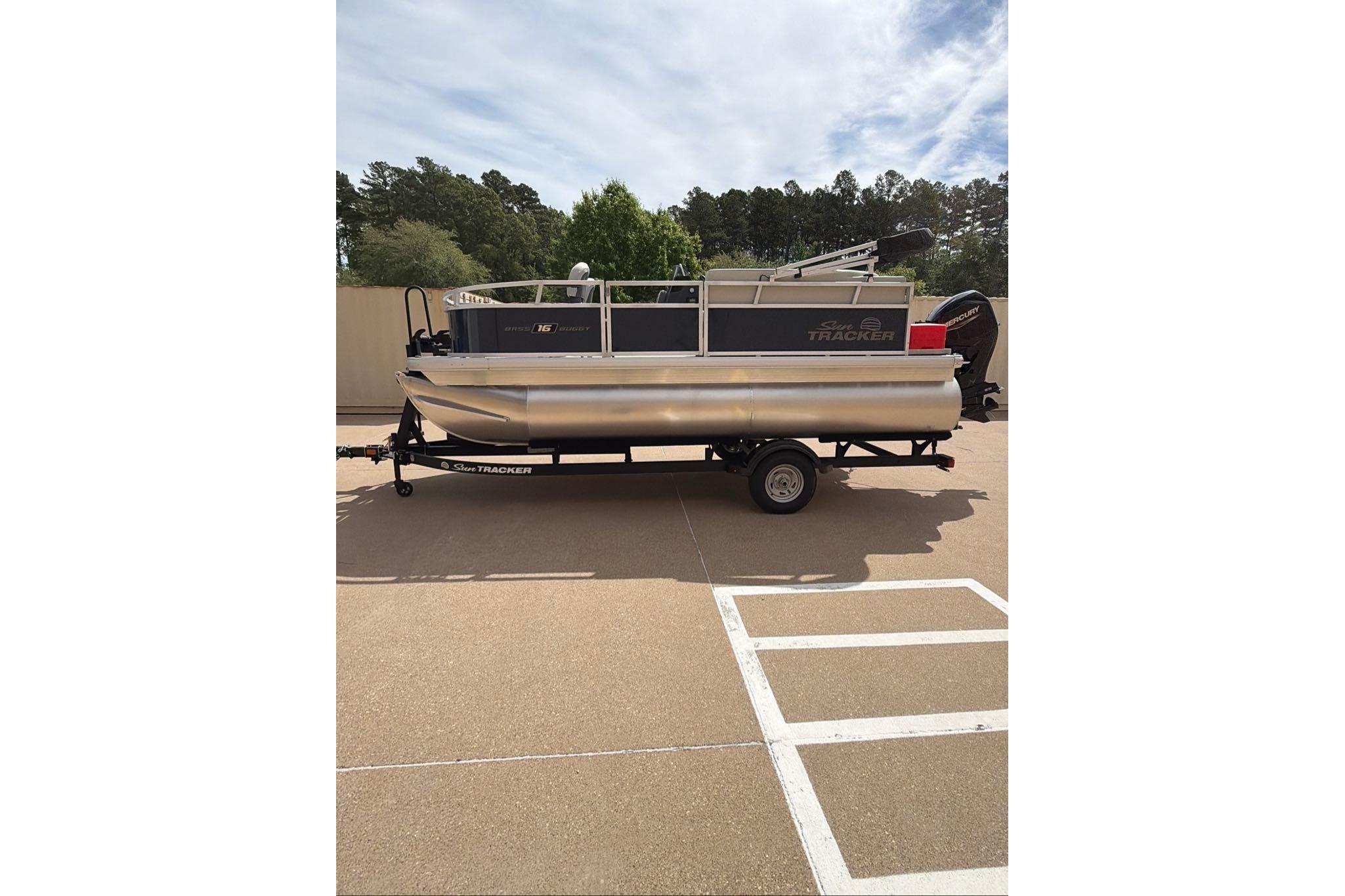 2026 Sun Tracker Bass Buggy 16 XL Select pontoon boat on trailer, parked outdoors.