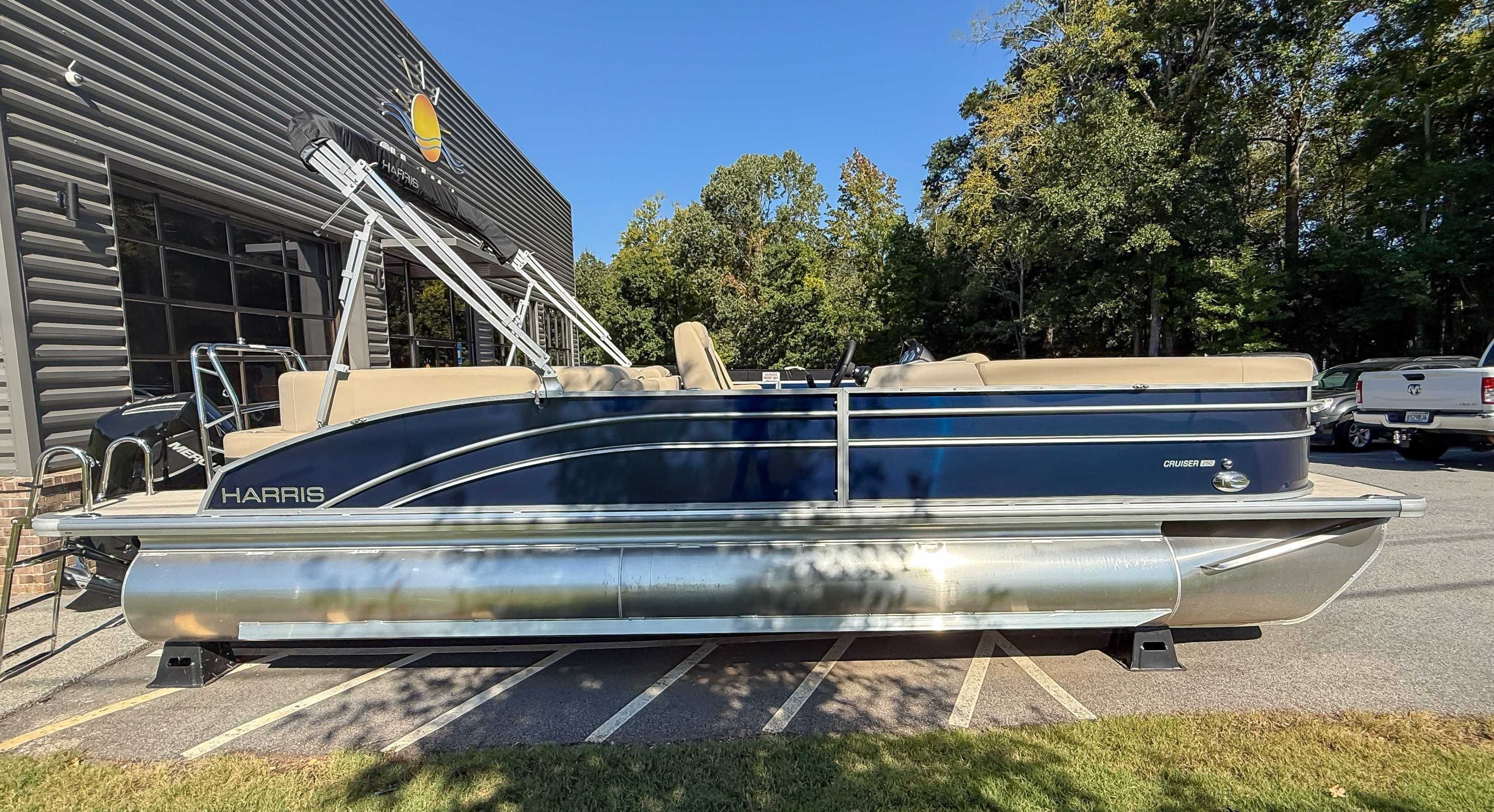 Harris Cruiser 250 CWDH 2025 pontoon boat parked outside a building.