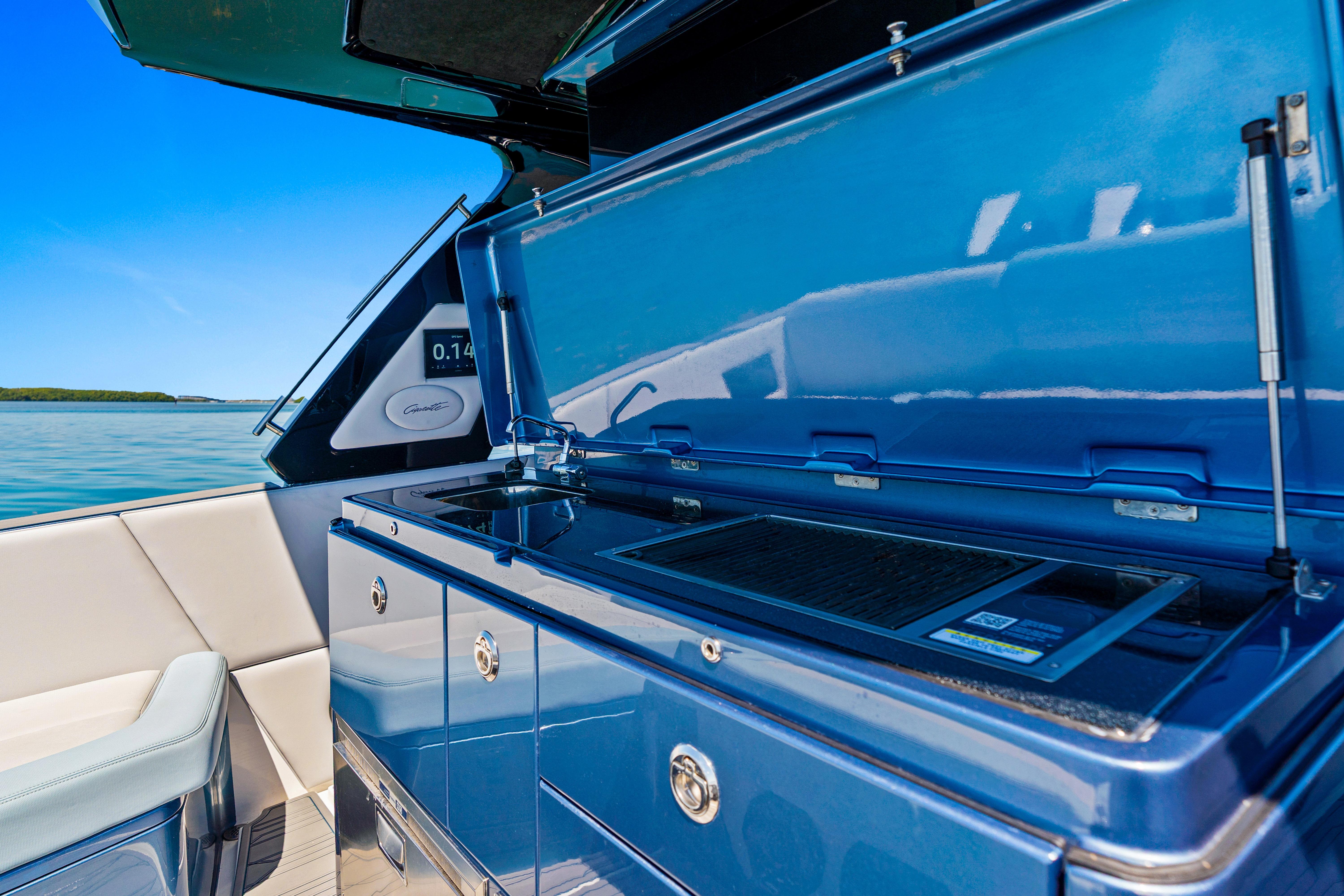 Outdoor kitchen on 2024 Cigarette 42' Auroris boat with blue cabinetry and scenic water view.