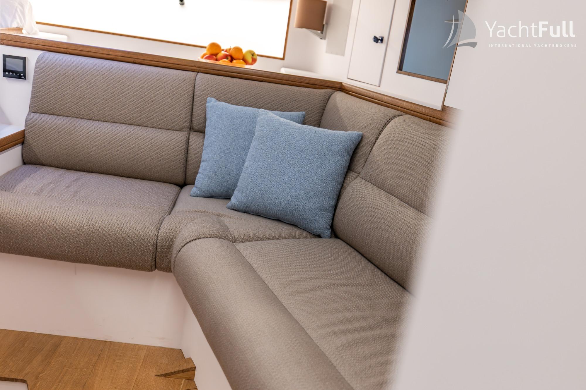 Cozy interior of 1987 Nordia Van Dam 82 ketch with beige seating and blue cushions.