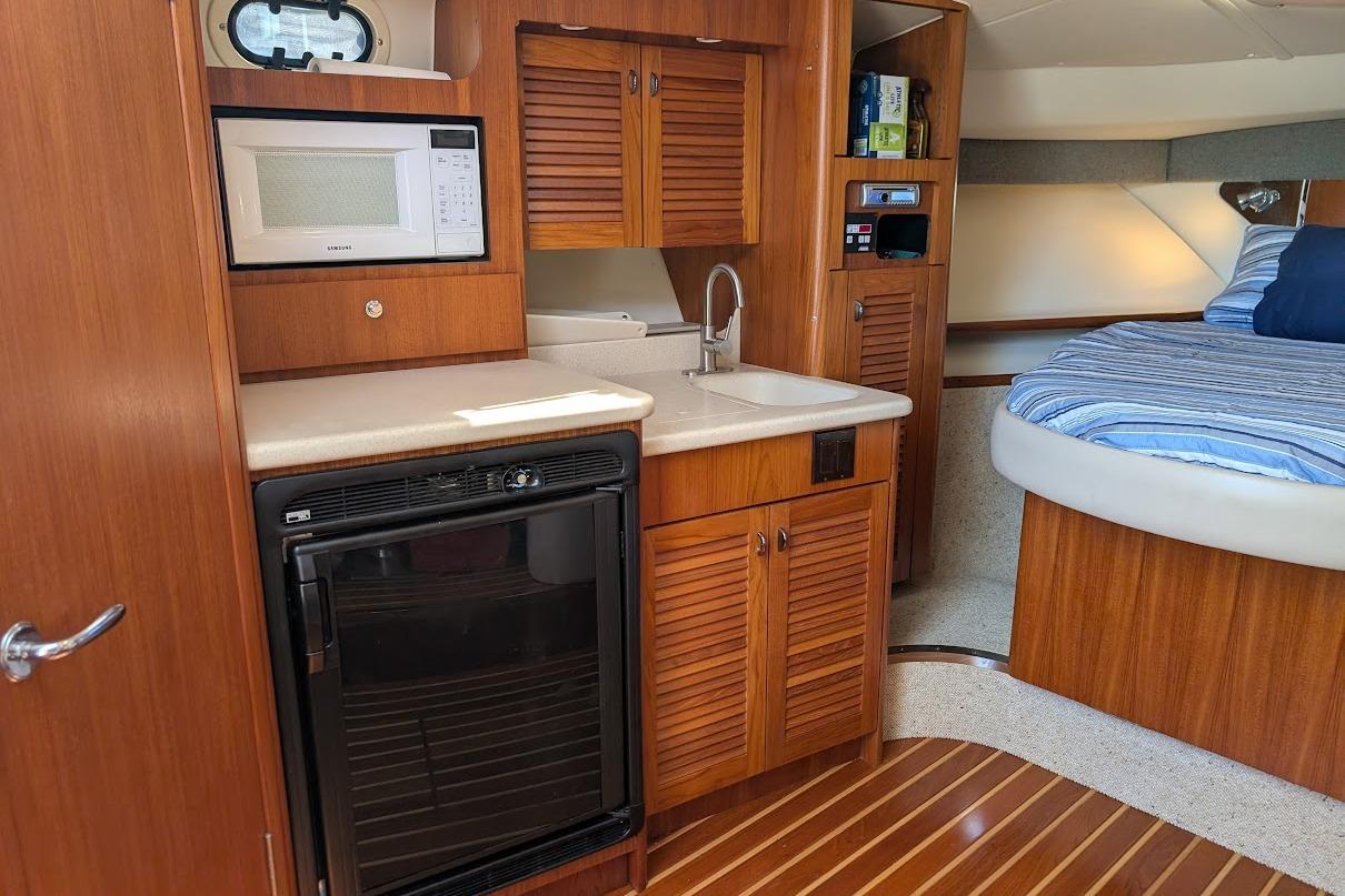 2000 Pursuit 3400 Express cabin interior with kitchenette and bed, featuring wood cabinetry and flooring.