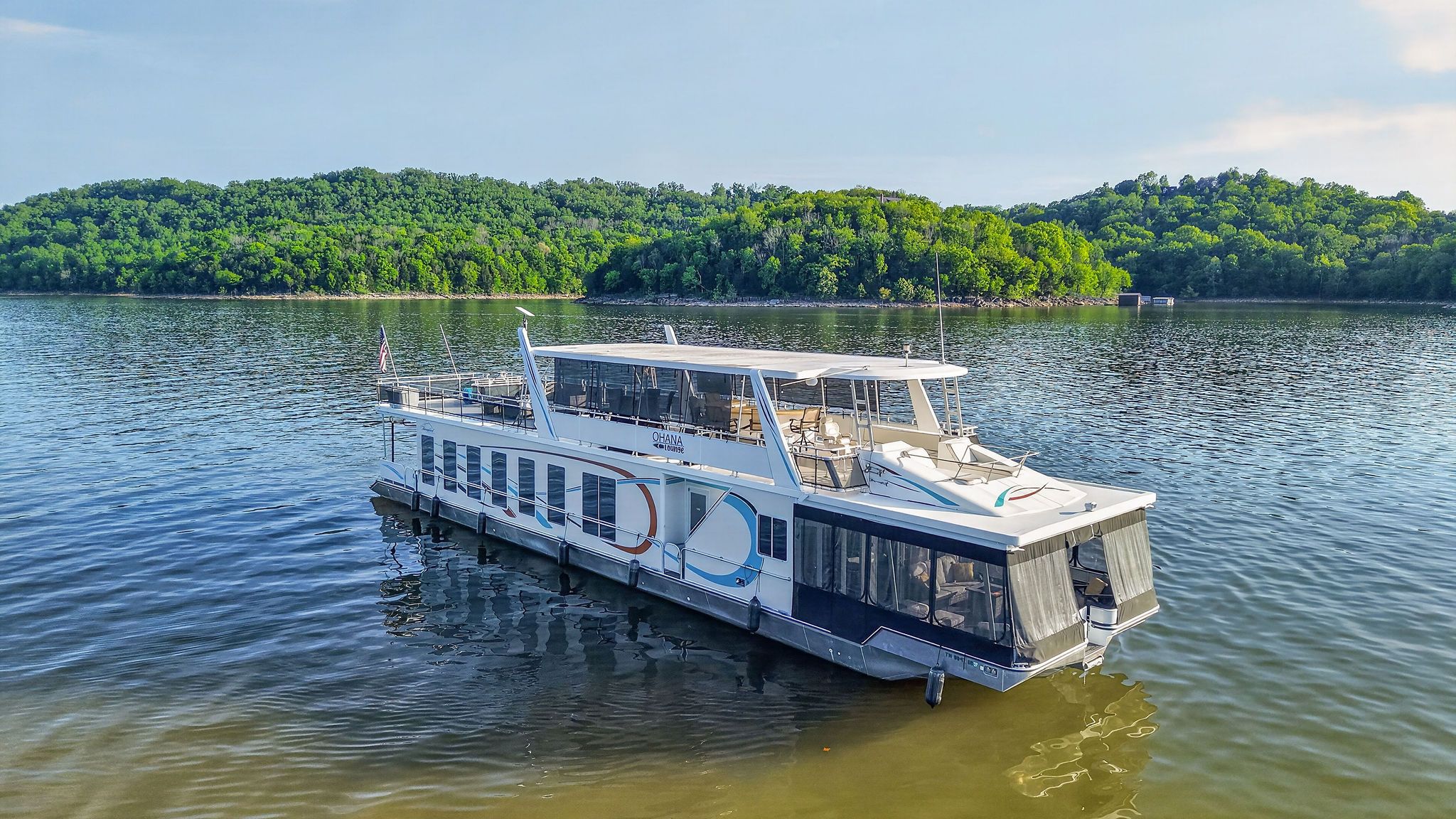 Houseboat on a serene lake with wooded hills in the background.