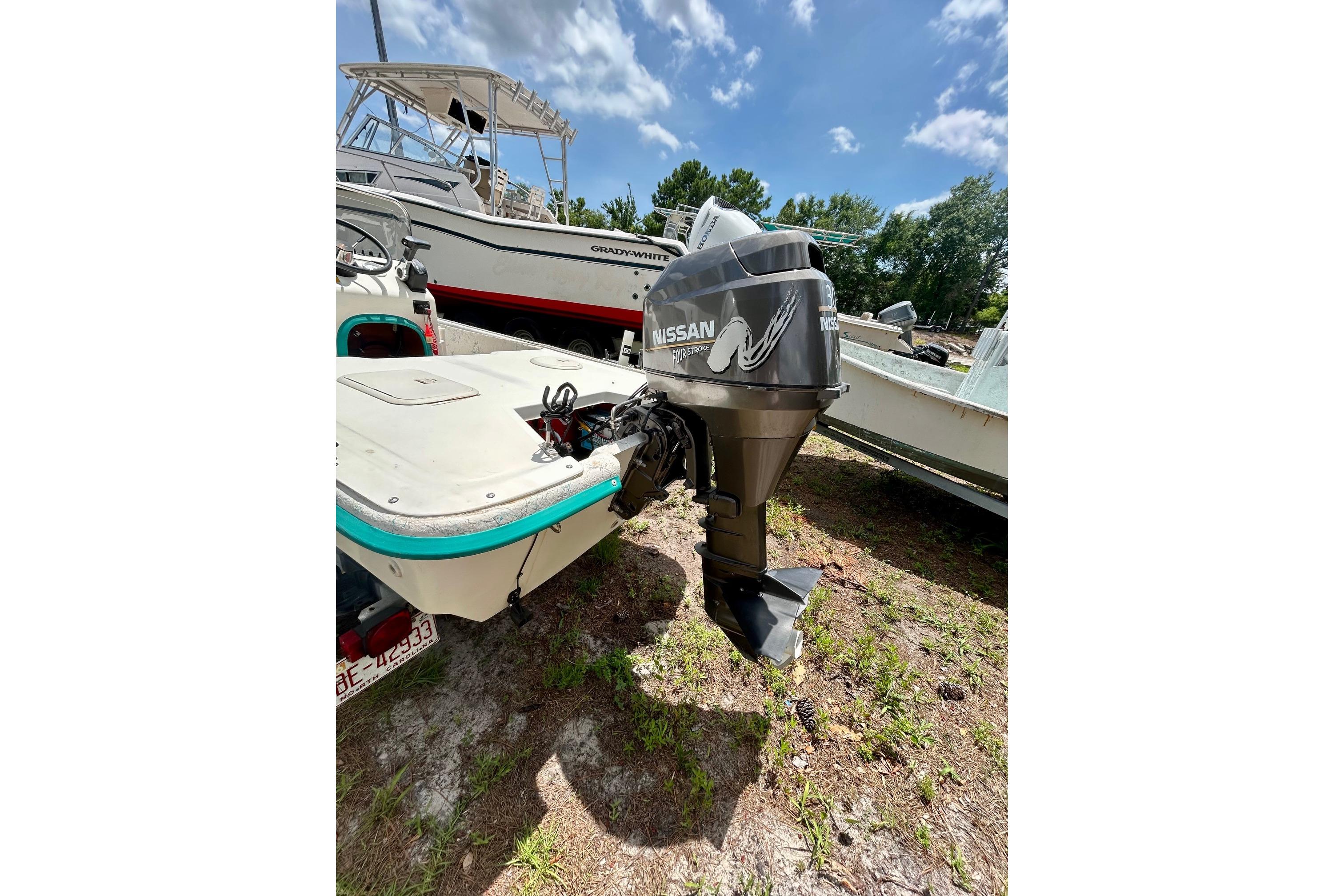 2002 Sundance K16CC boat with Nissan outboard motor, parked on grass under blue sky.