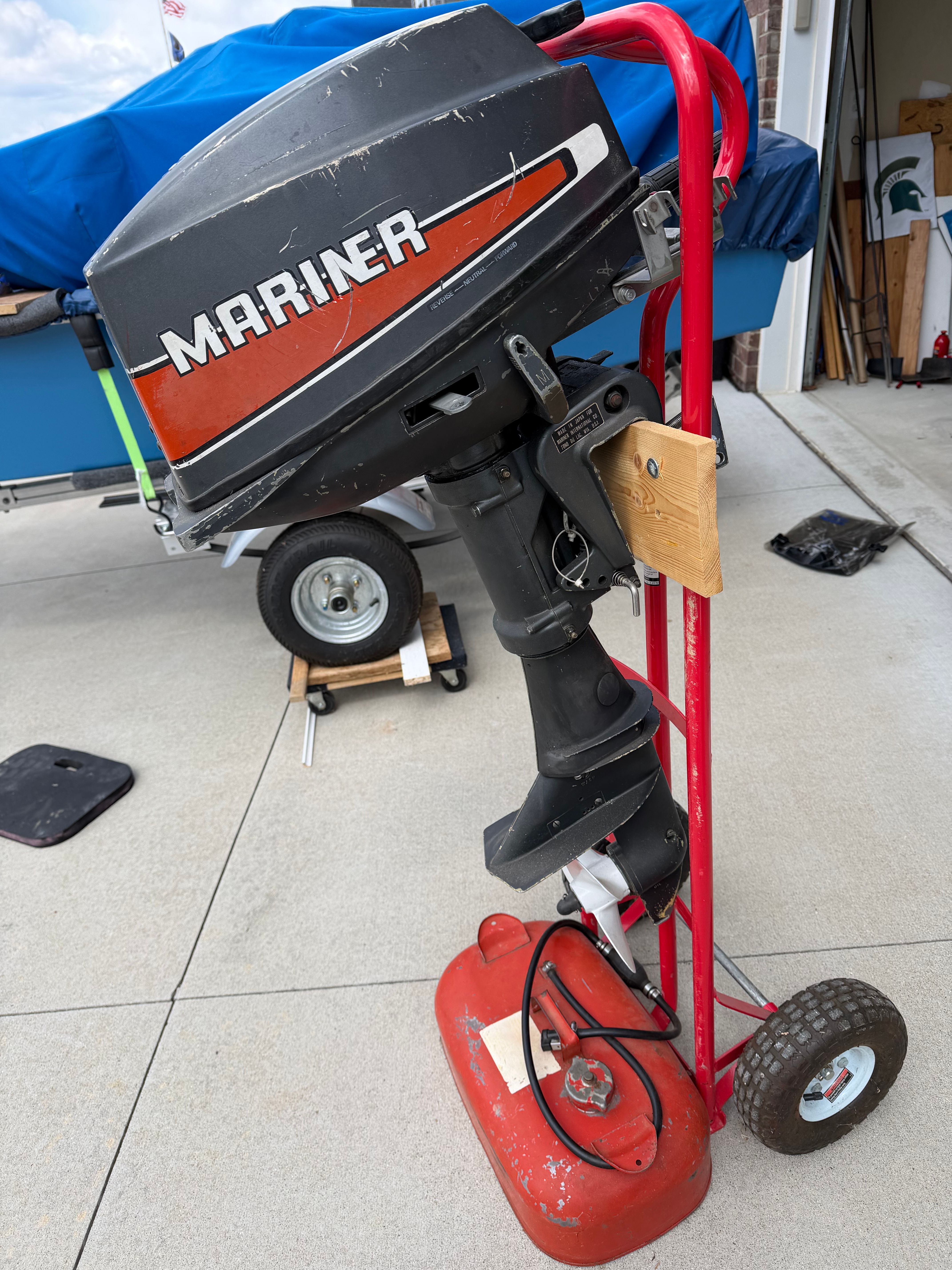 An outboard motor on a red dolly, with a blue boat in the background.