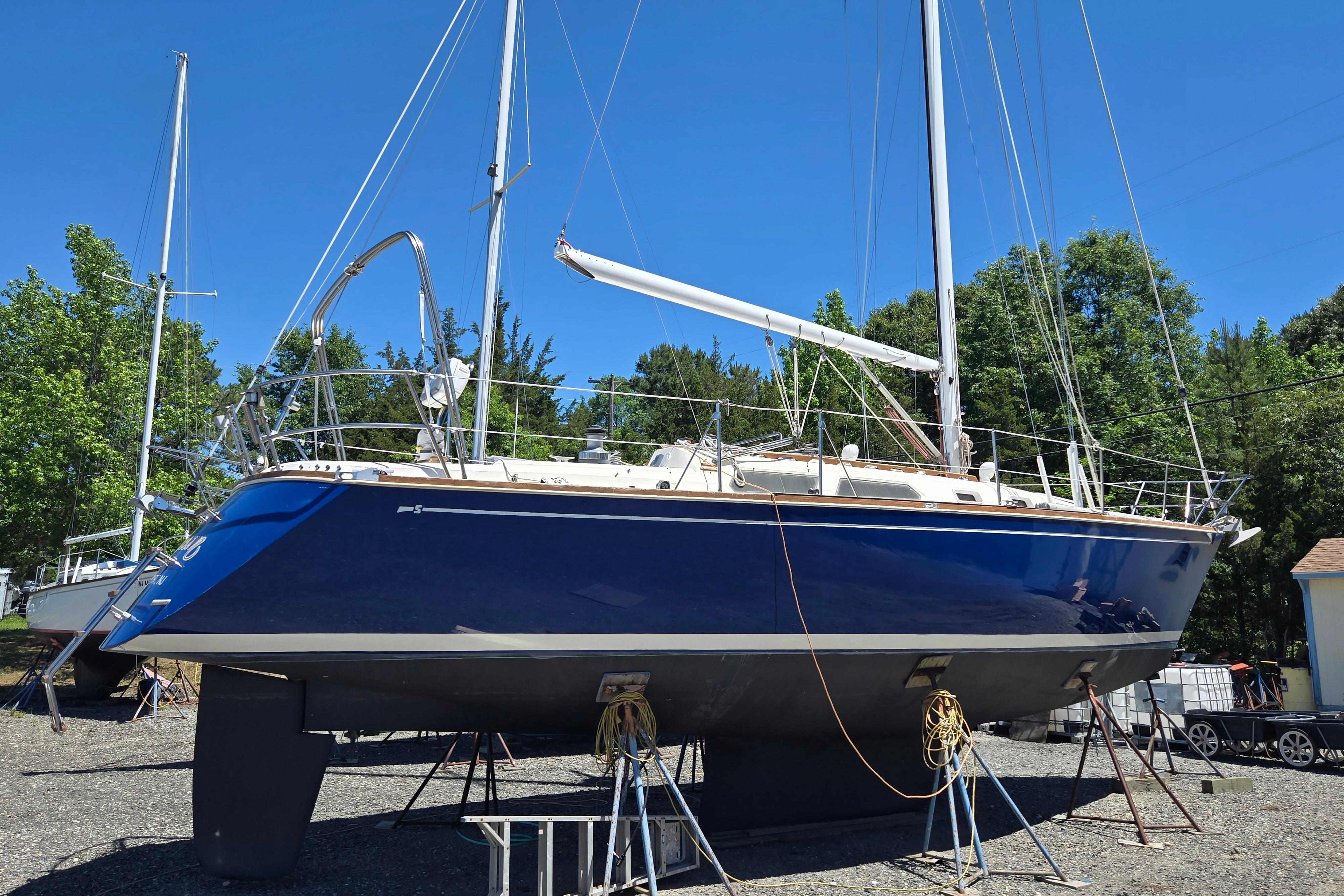 1988 Sabre 38 sailboat on land, blue hull, mast up, surrounded by trees.