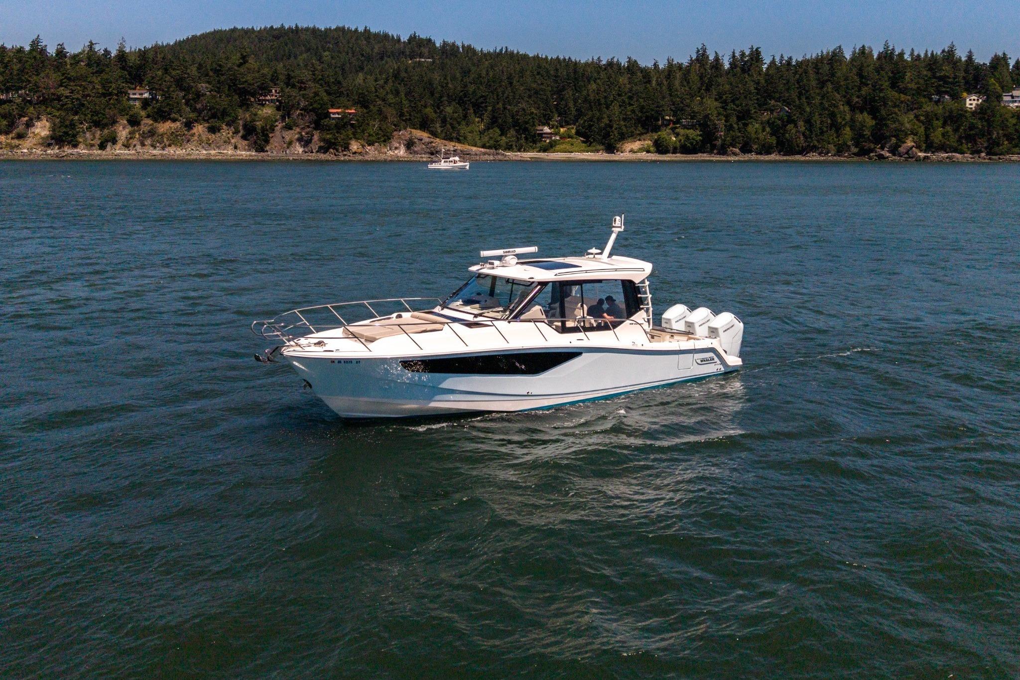 2023 Boston Whaler 405 Conquest cruising on a scenic lake with forested shoreline.