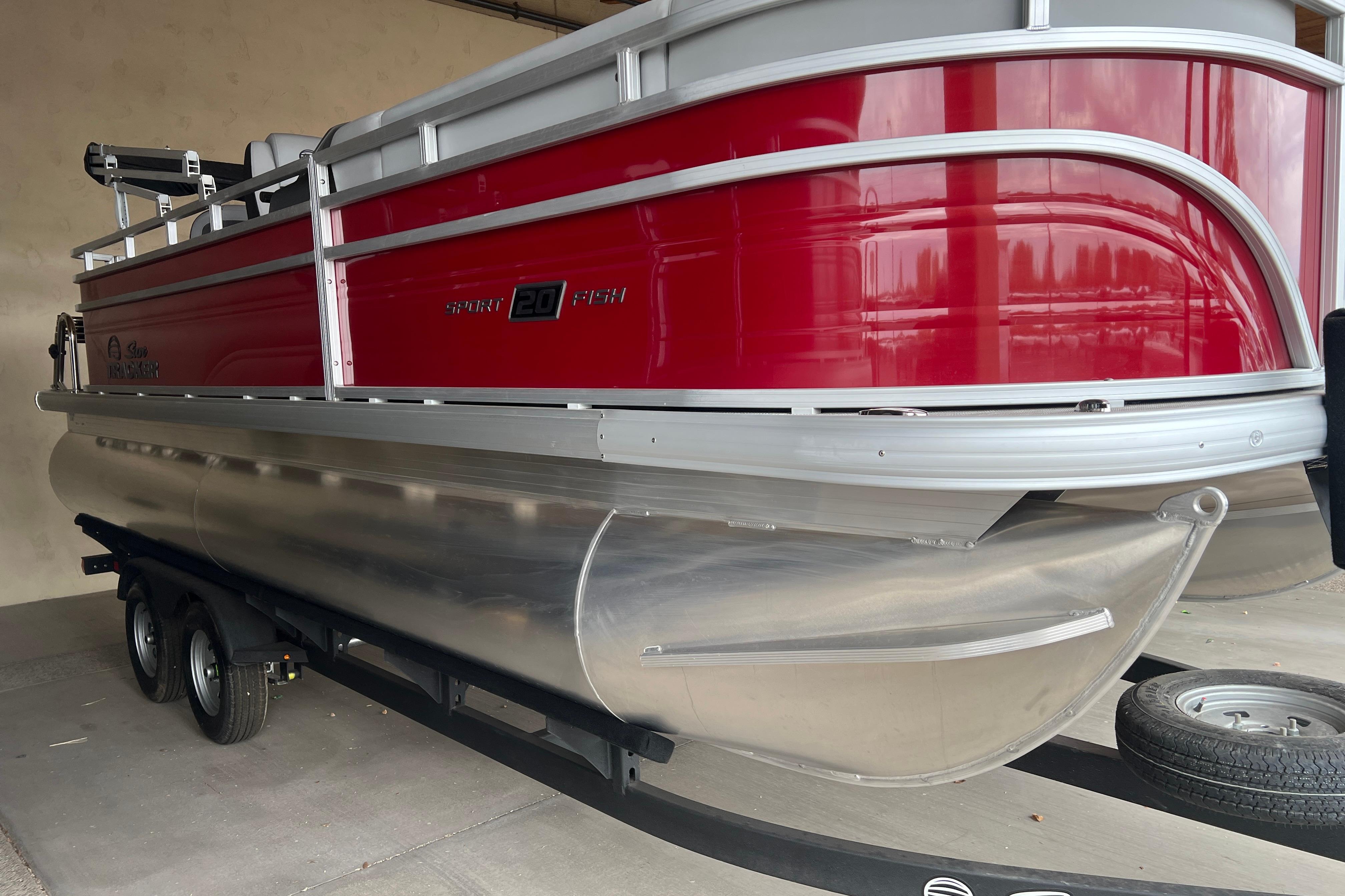 2026 Sun Tracker SportFish 20 DLX pontoon boat with red and silver design on trailer.