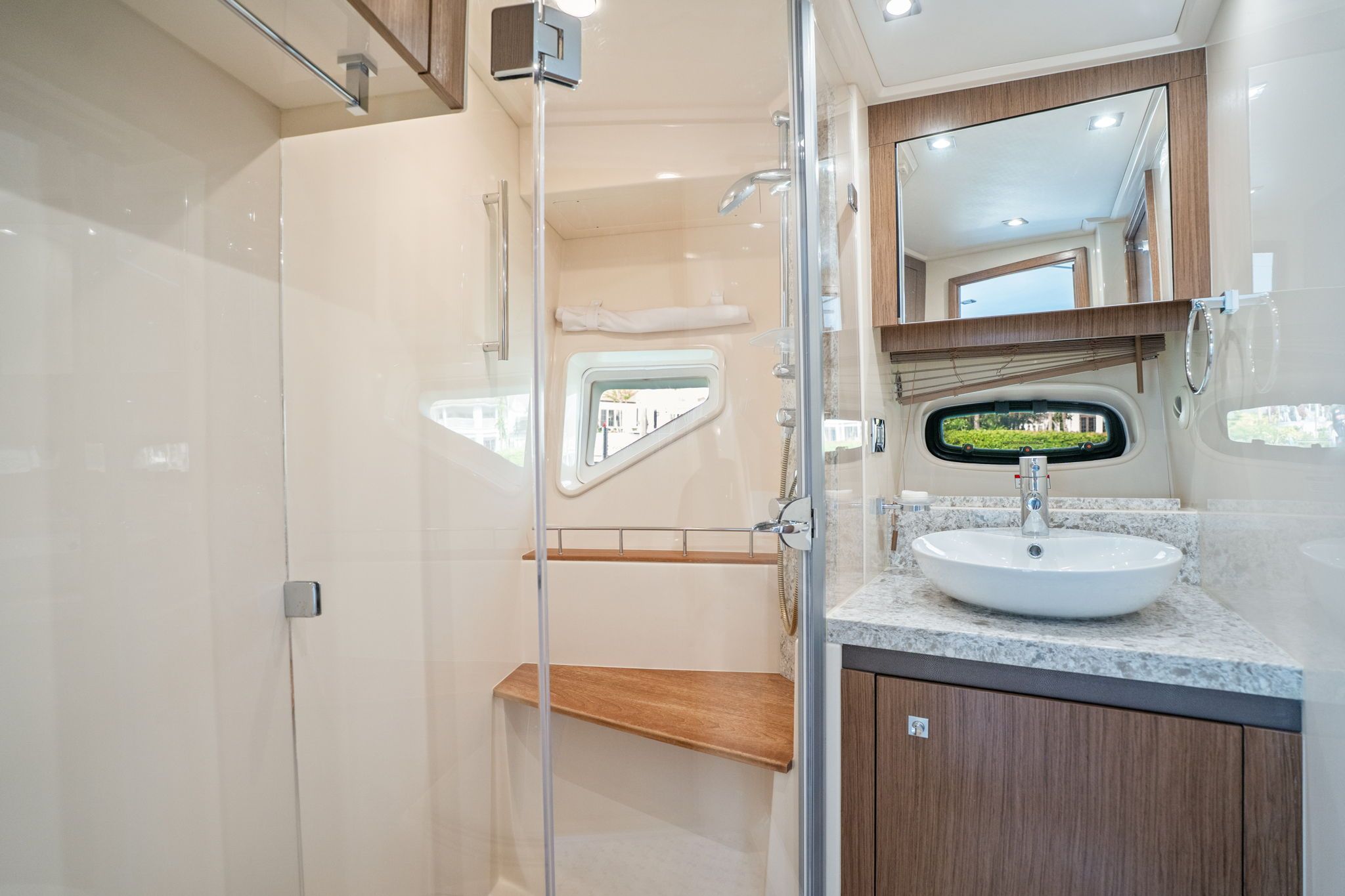 The image shows a modern yacht bathroom with a sink, mirror, and shower.