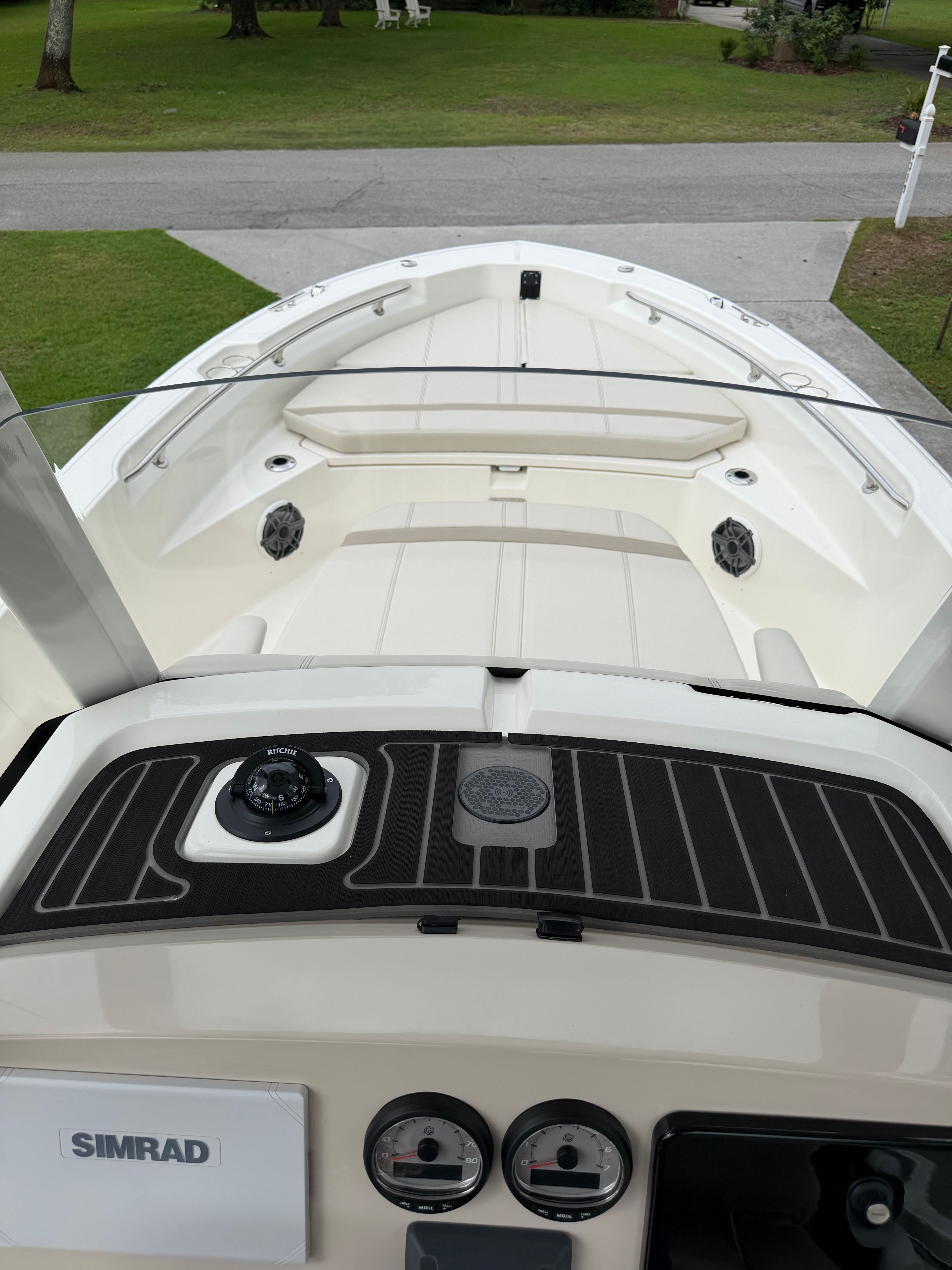 The image shows the deck of a 2025 Boston Whaler 220 Dauntless boat. It features a clean, modern design with a Simrad display and various instruments.
