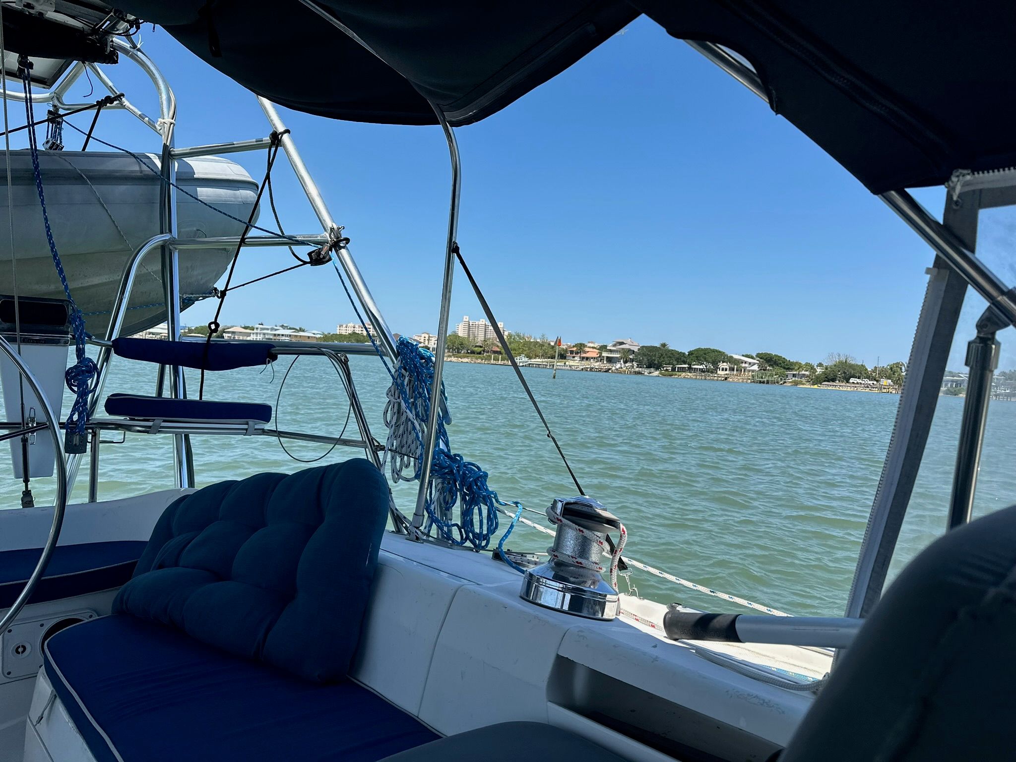 View from a sailboat overlooking calm water and a shoreline in the background.