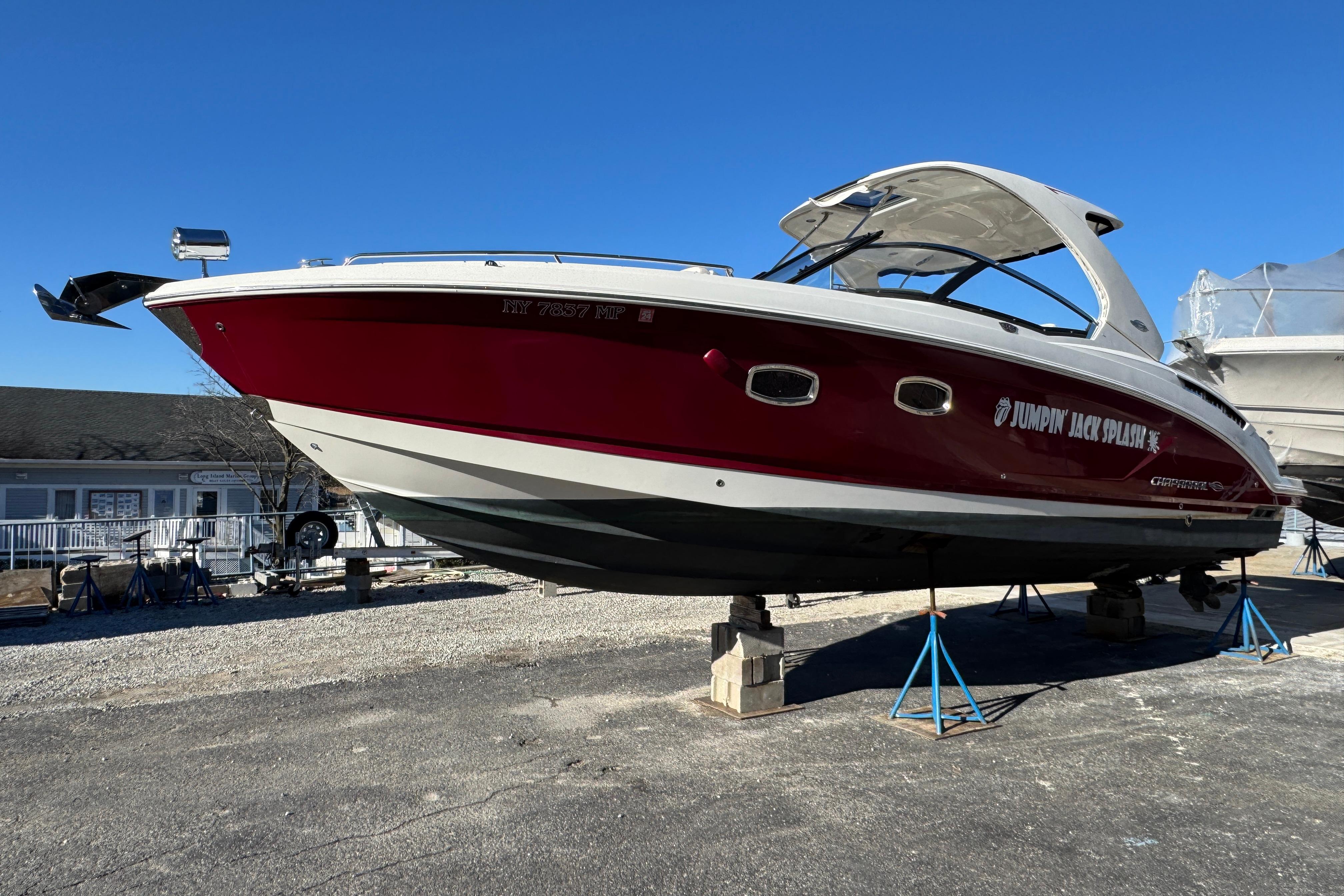 2012 Chaparral 327 SSX boat on stands, red and white hull, clear blue sky.
