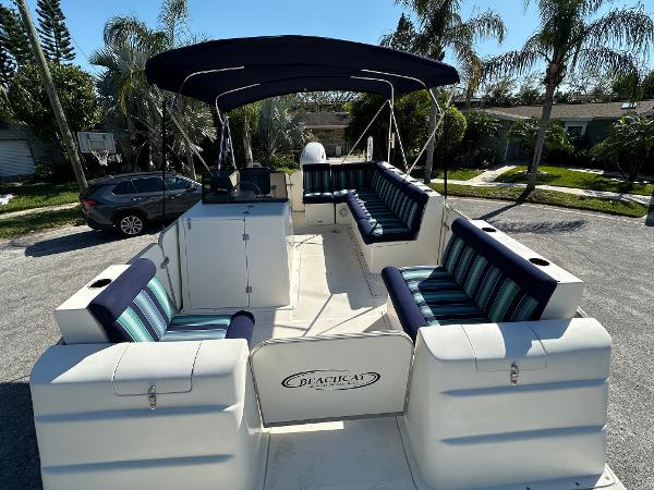 2020 Beachcat 20 boat with striped seating and canopy, parked near palm trees.