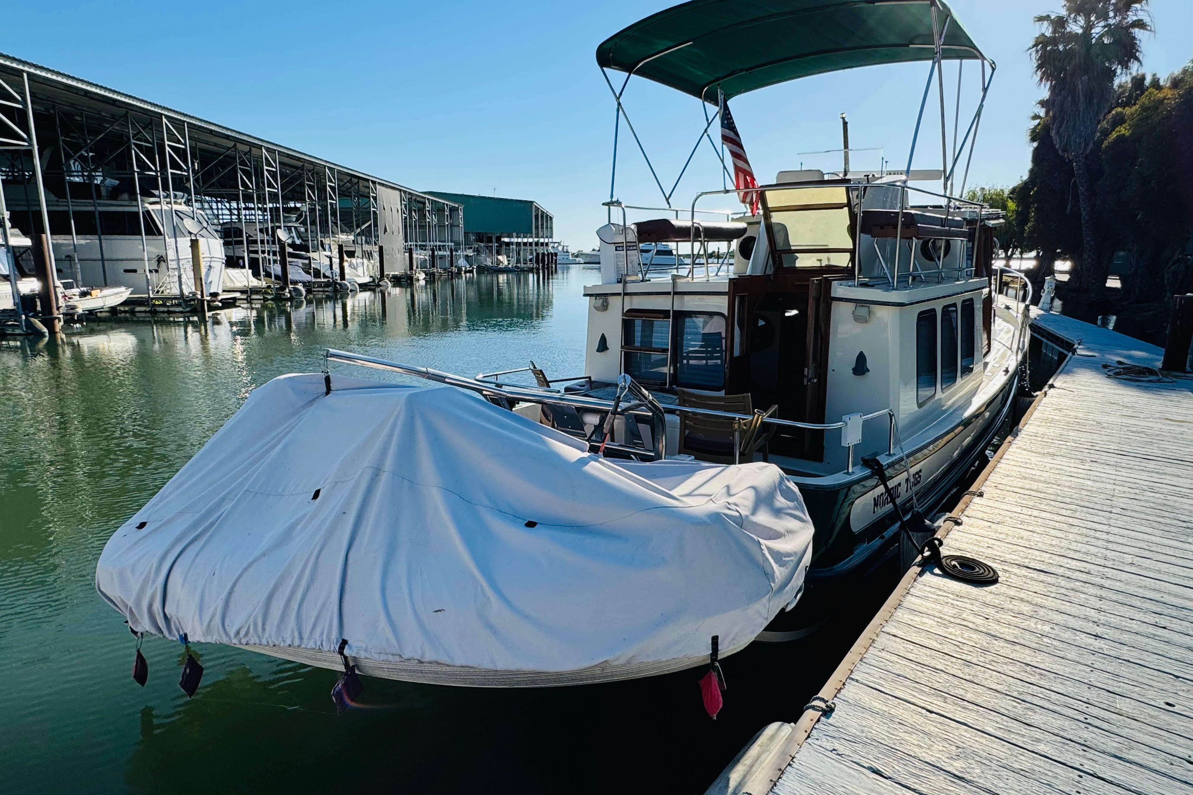 1996 Nordic Tug 32 docked at marina, covered dinghy, sunny day, calm water.