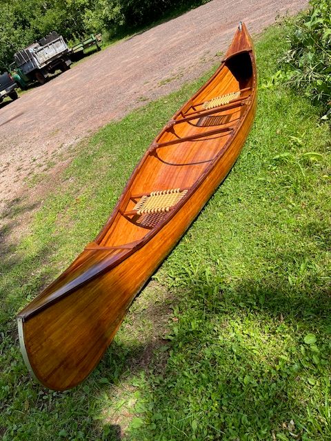 A handcrafted cedar strip canoe rests on a grassy area.