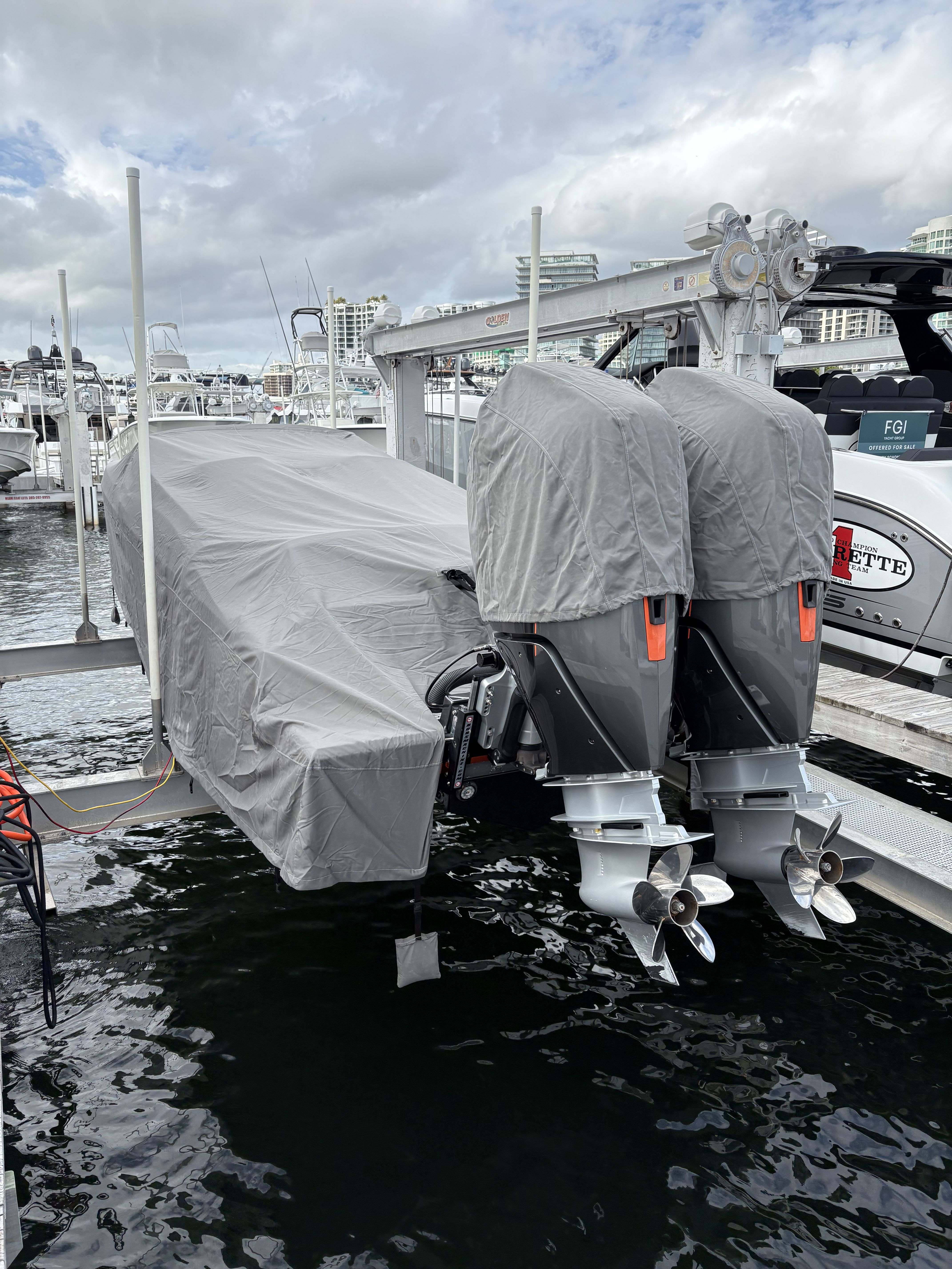 A boat covered with tarps and two outboard motors is docked at a marina.