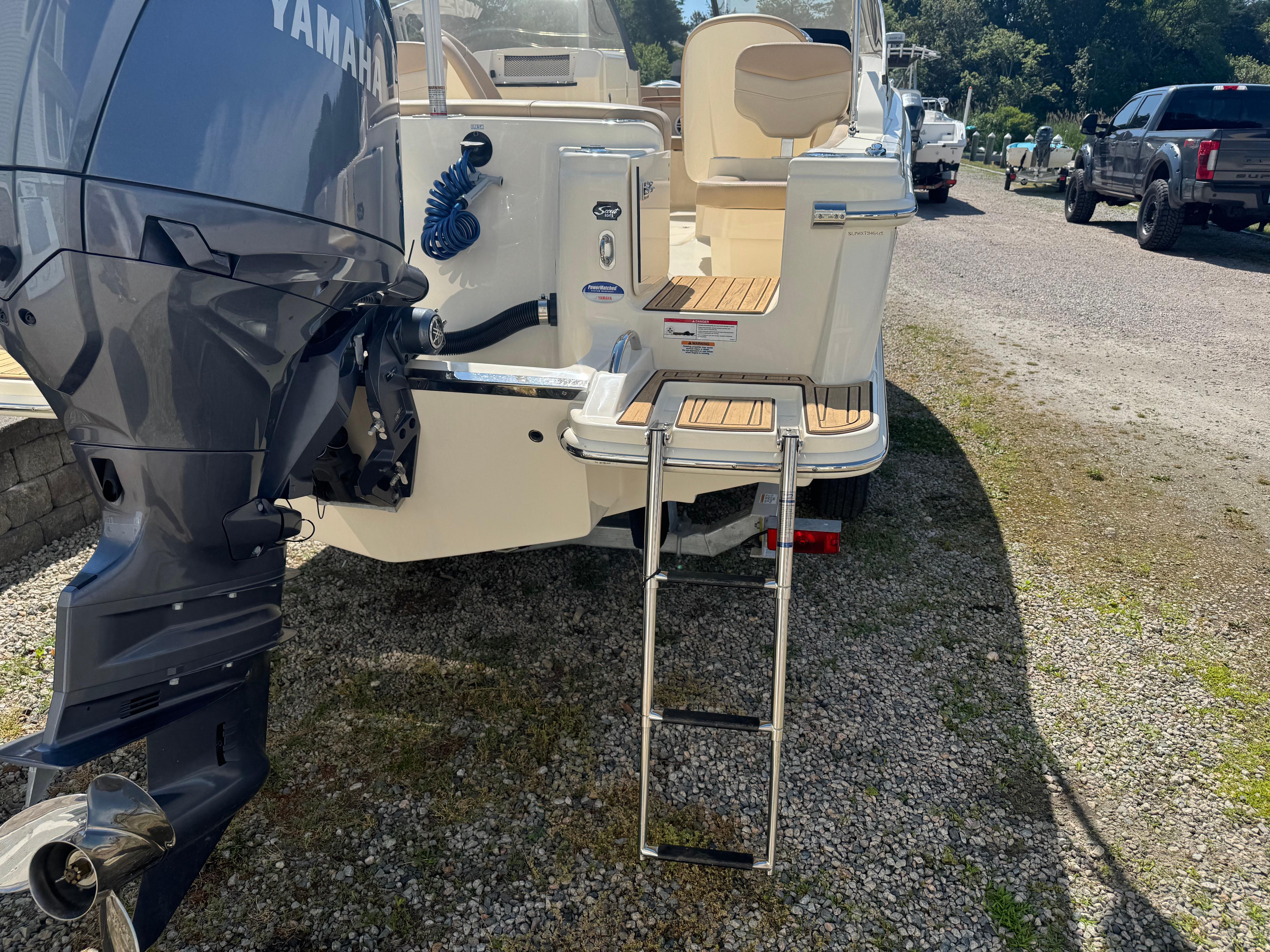 2025 Scout 215 Dorado boat with Yamaha outboard motor and swim ladder on gravel.