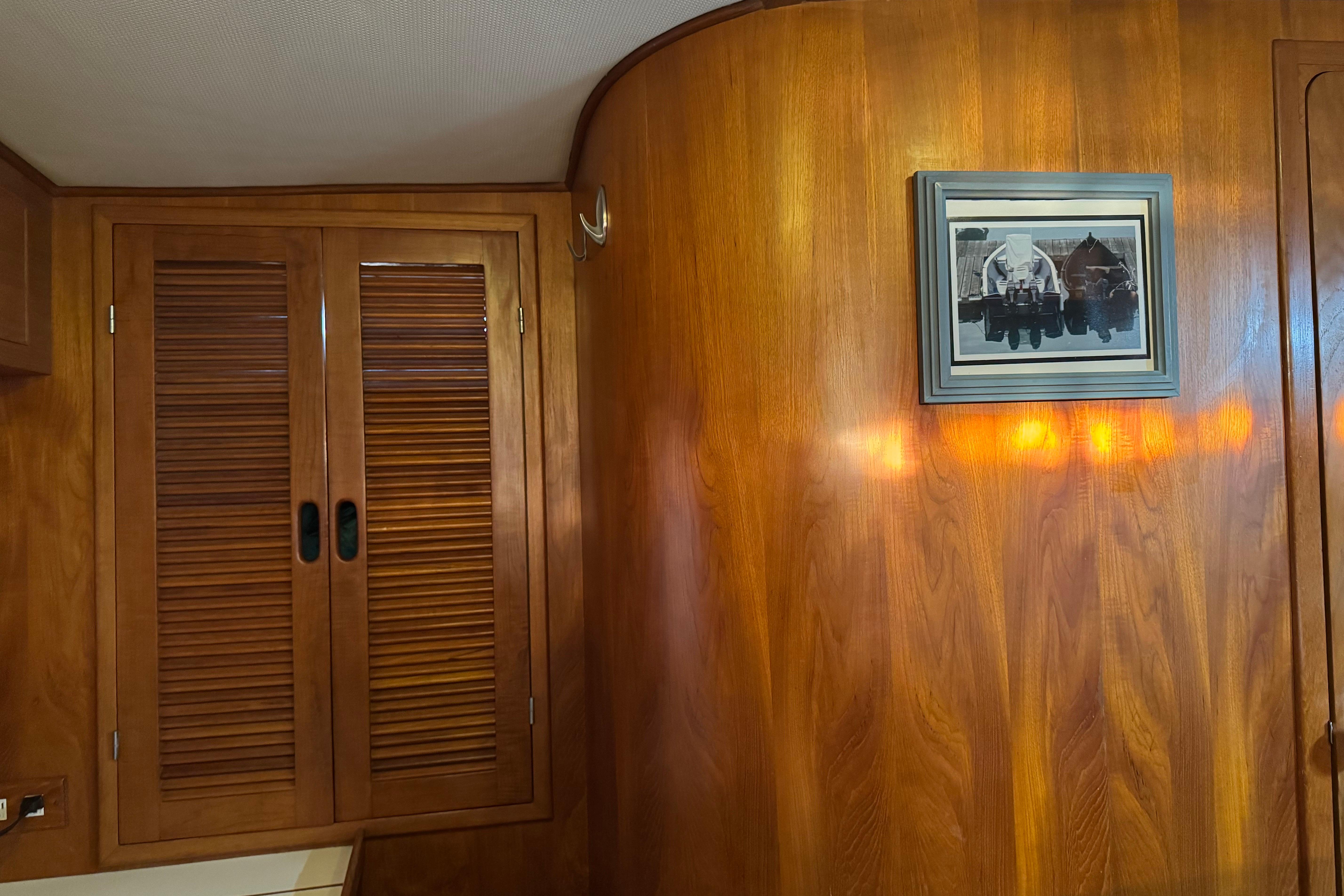 Wood-paneled interior of a 1987 President 37 yacht with framed artwork and louvered cabinet doors.