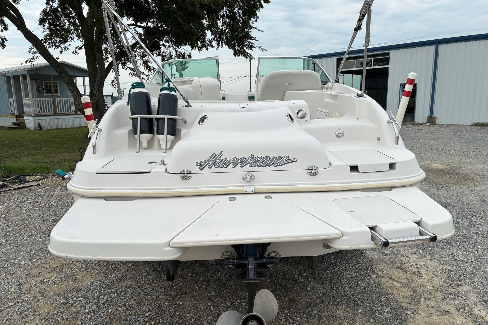 2003 Hurricane 234 SD boat, rear view, parked on gravel near buildings and trees.