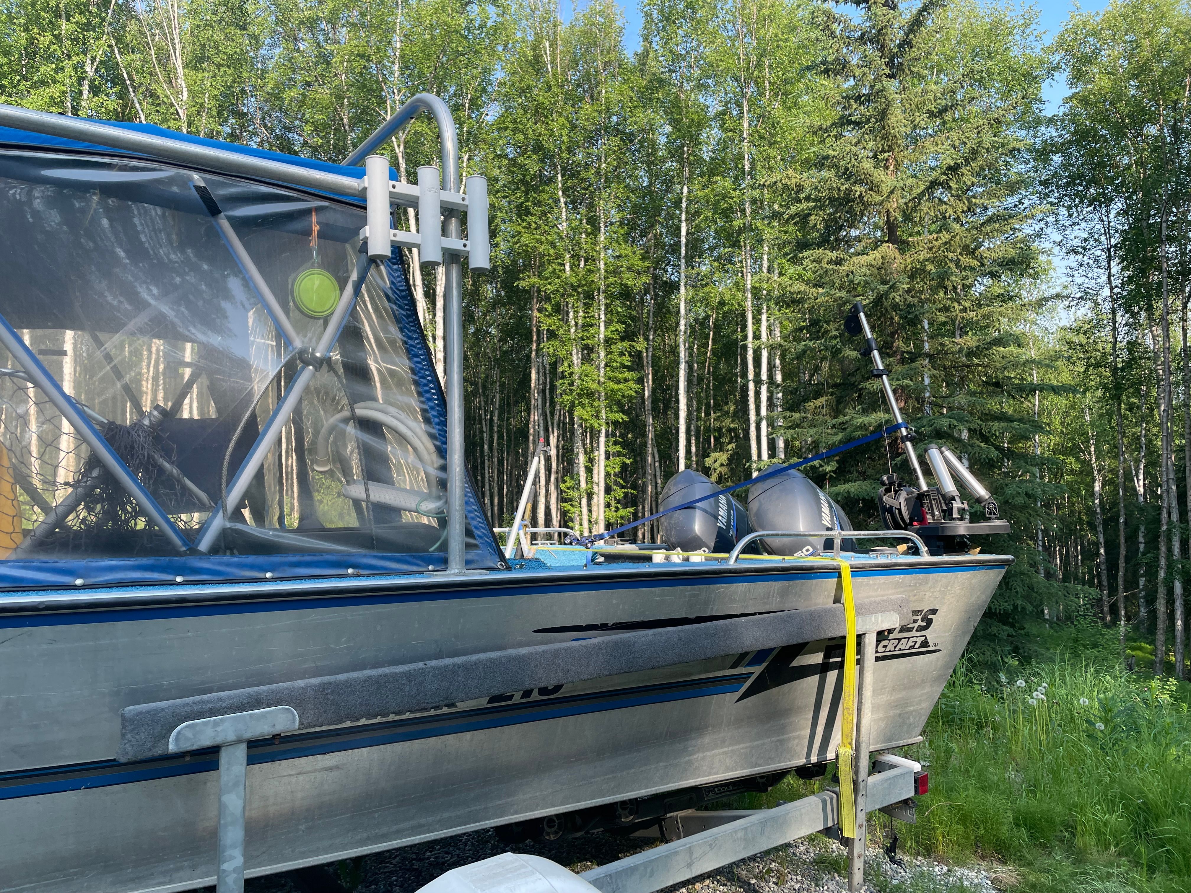 A 1998 Hewescraft Sea Runner 210 boat on a trailer in a wooded area.