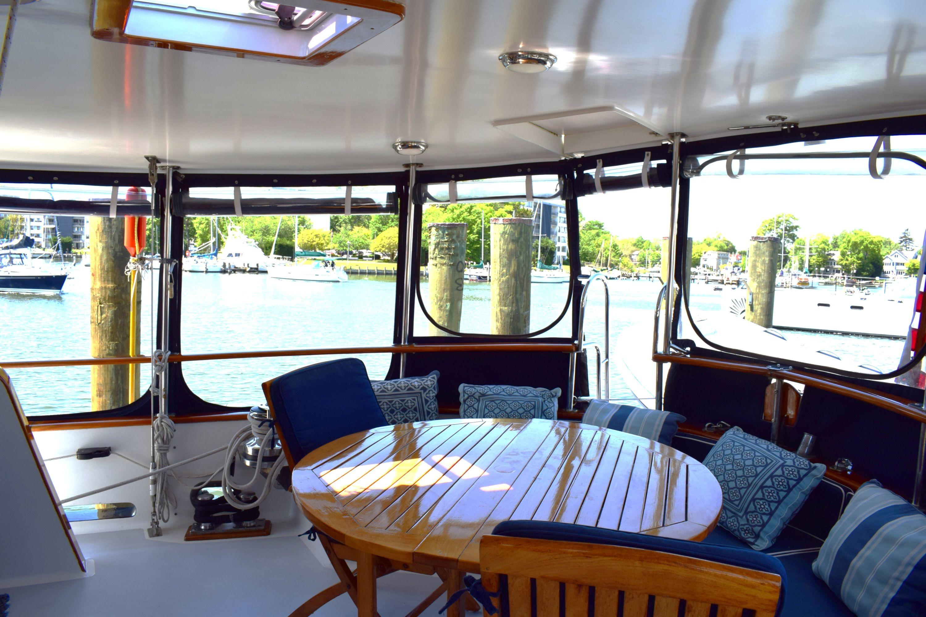 1980 Cheoy Lee 52 Motorsailer cockpit with wooden table, cushioned seating, and marina view.