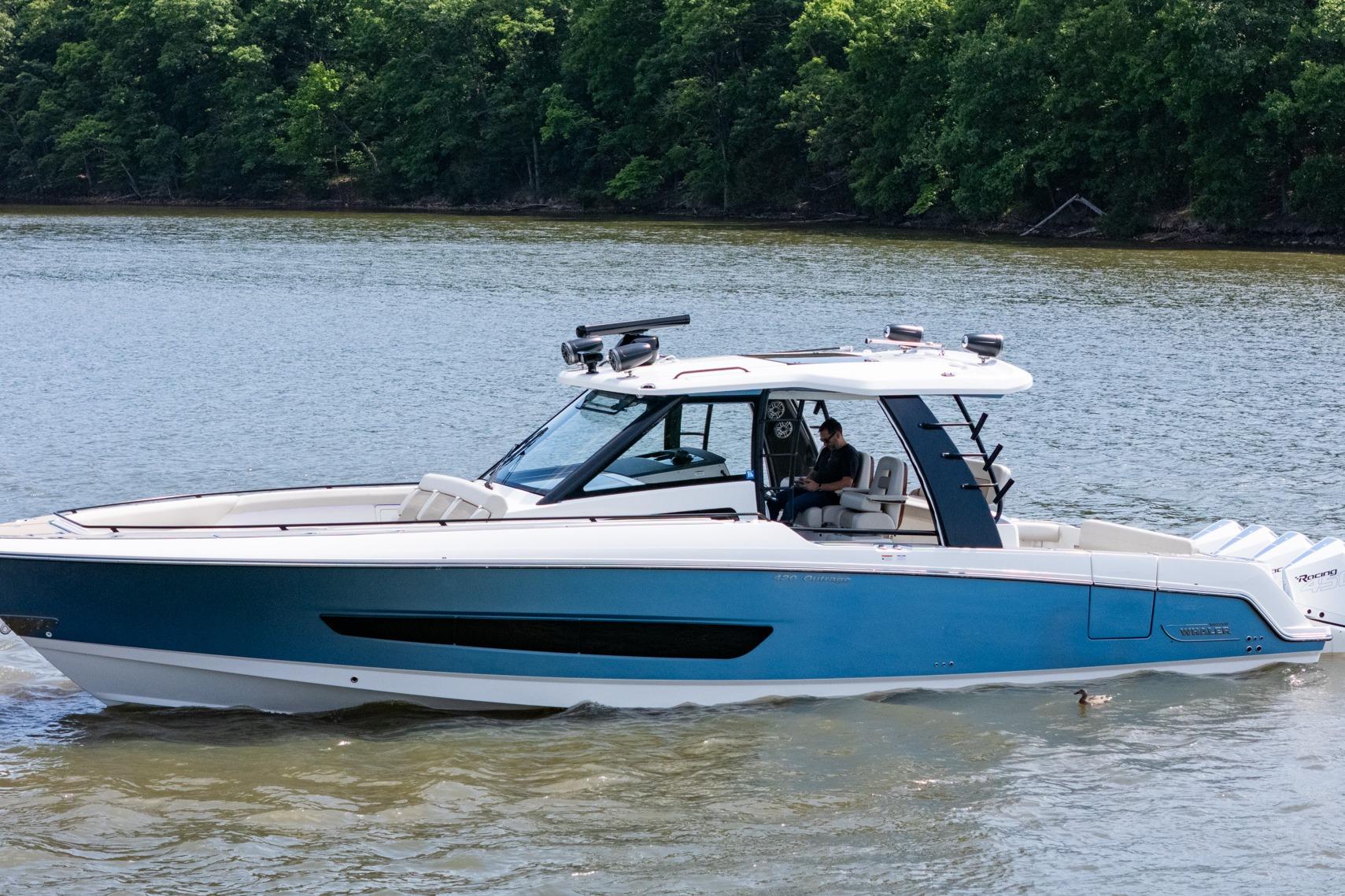 2021 Boston Whaler 420 Outrage boat cruising on a serene lake with lush green trees.