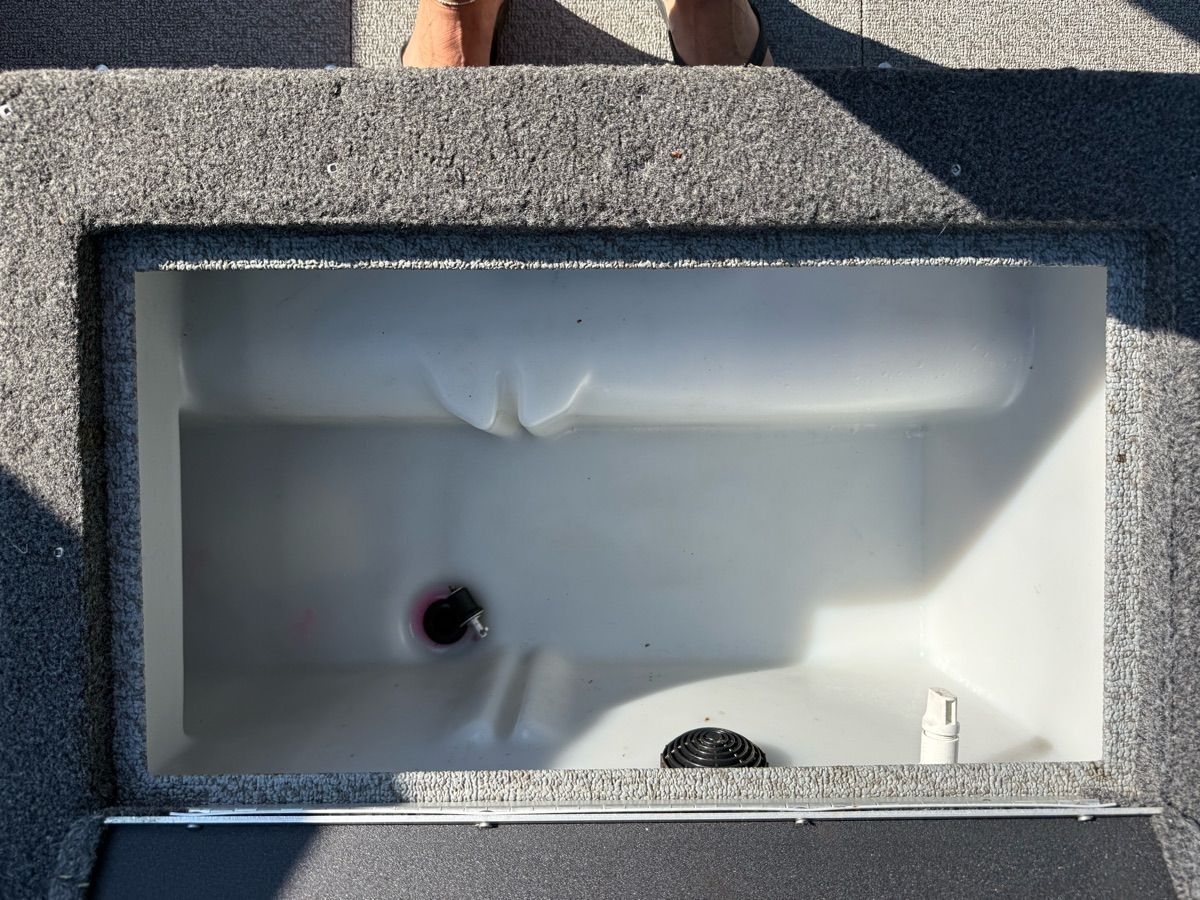 An open storage compartment on a boat with gray carpeted flooring.