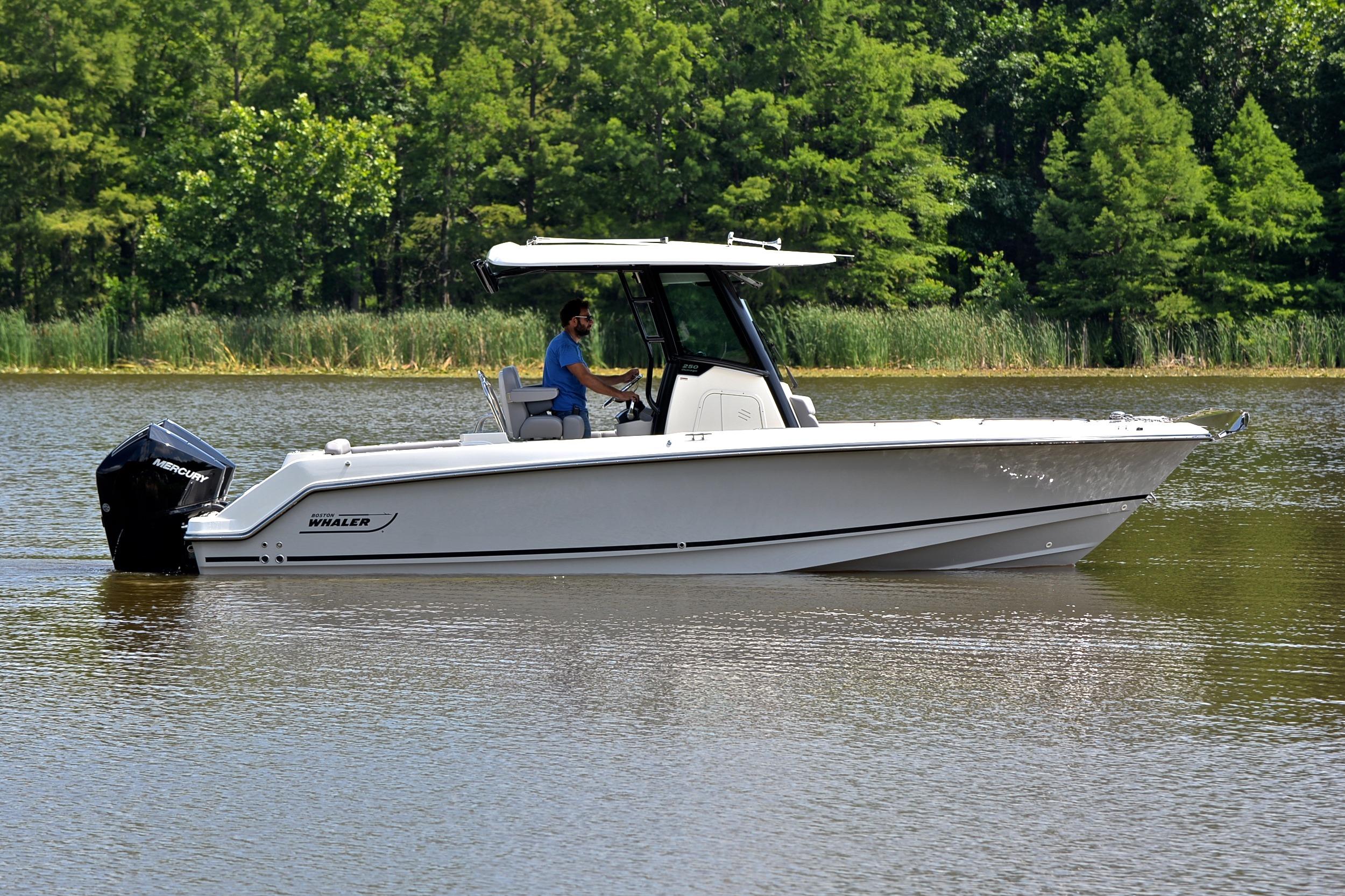 2024 Boston Whaler 250 Outrage boat cruising on a calm lake with lush green trees.