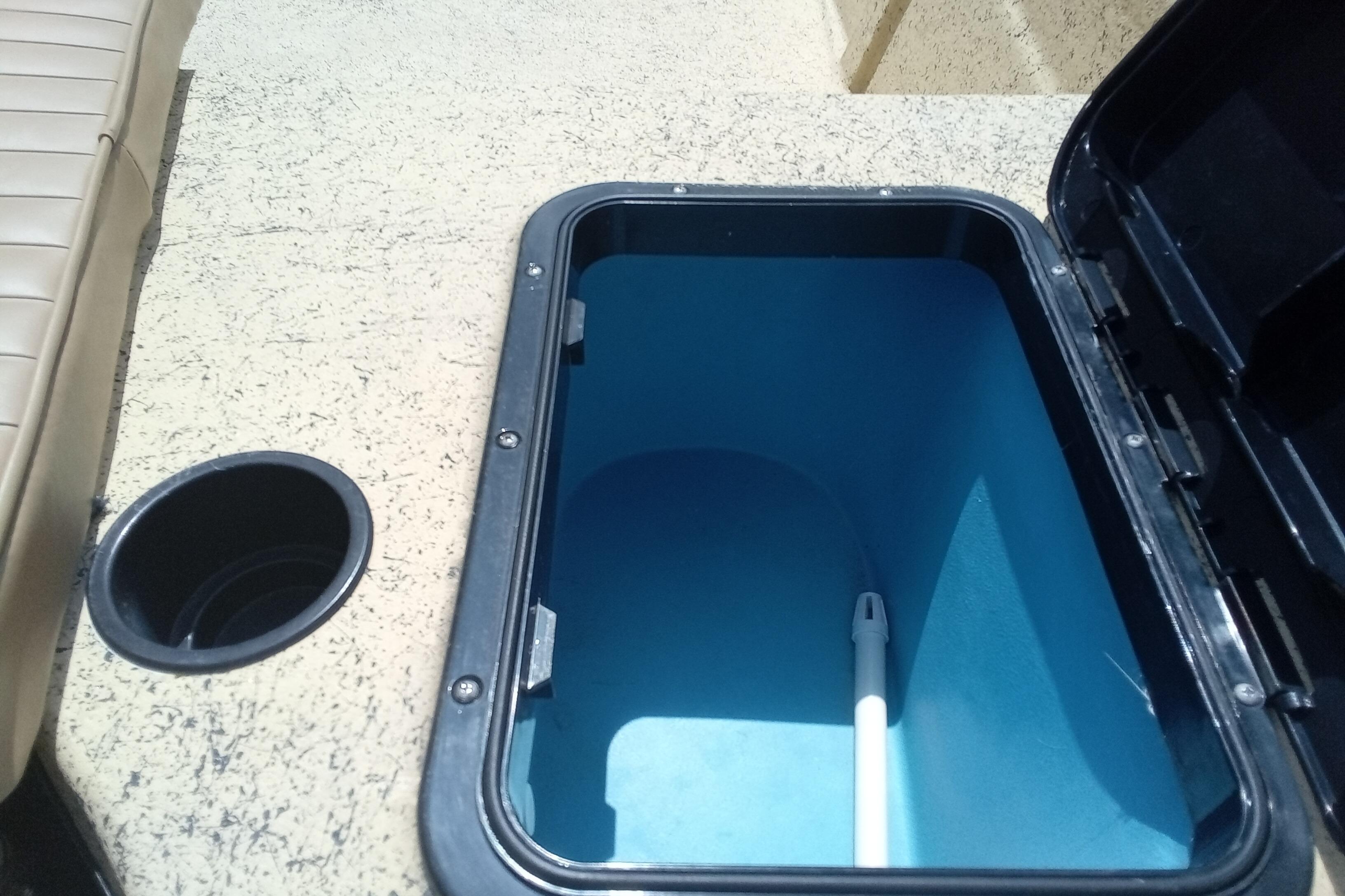 Open storage compartment on 2025 Fibercraft F16 boat with beige seating.