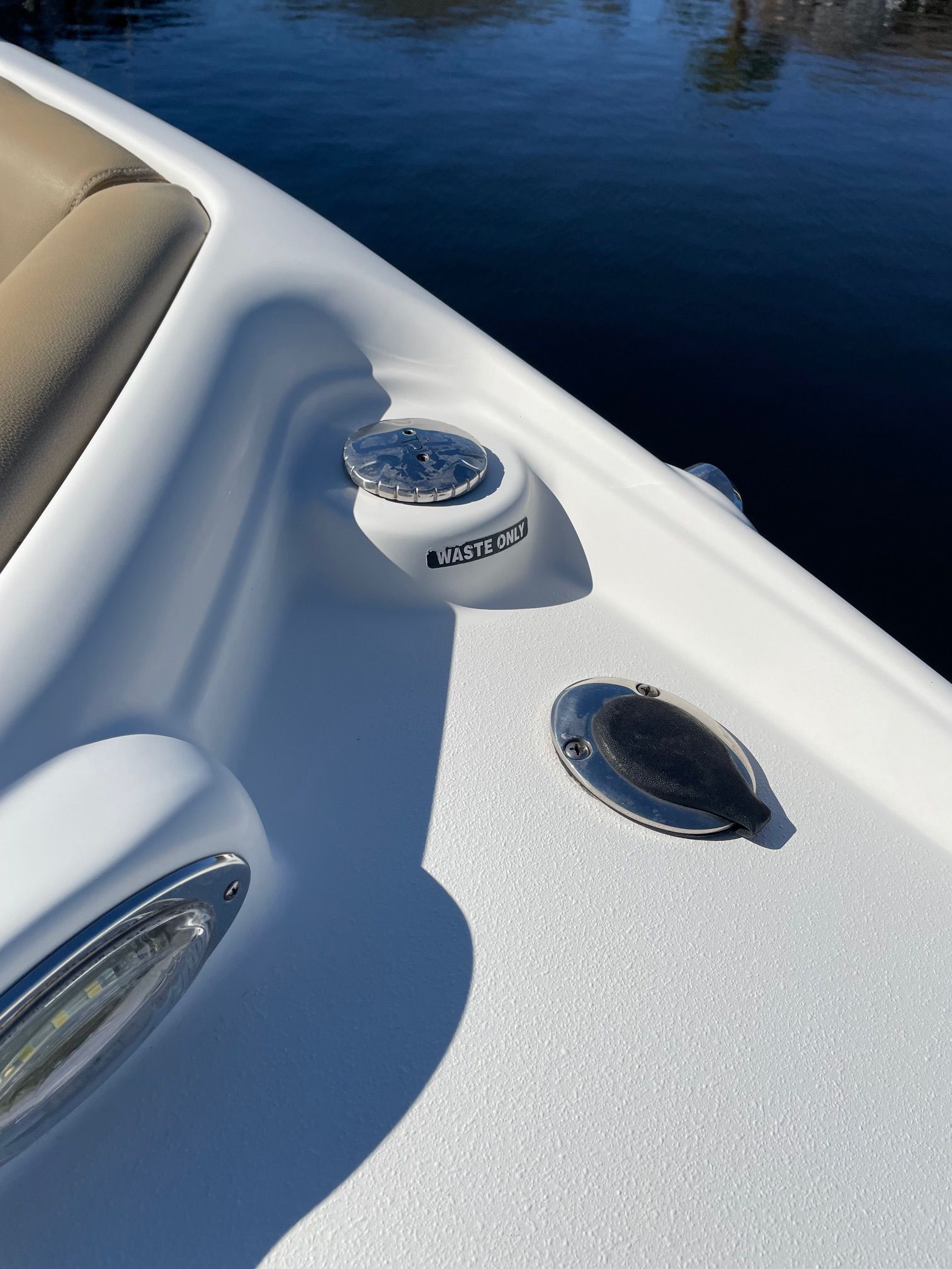 Close-up of a white boat deck with waste opening and water in the background.