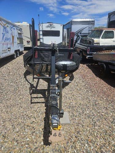 A boat trailer is parked on a gravel lot, surrounded by RVs and vehicles.
